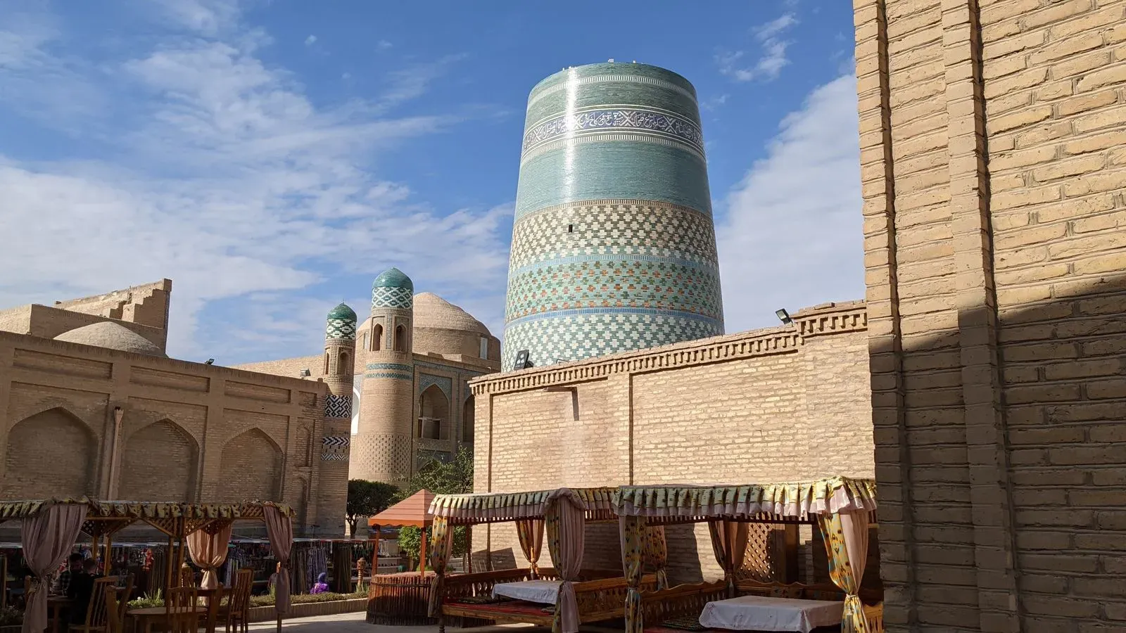 The iconic blue-tiled Kalta Minor Minaret in Khiva, surrounded by historic Islamic architecture and markets.