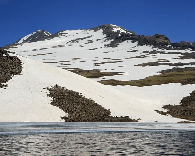 Snow-covered Kari Lake on Mount Aragats, Armenia, reflecting the rugged peaks under a clear blue sky.