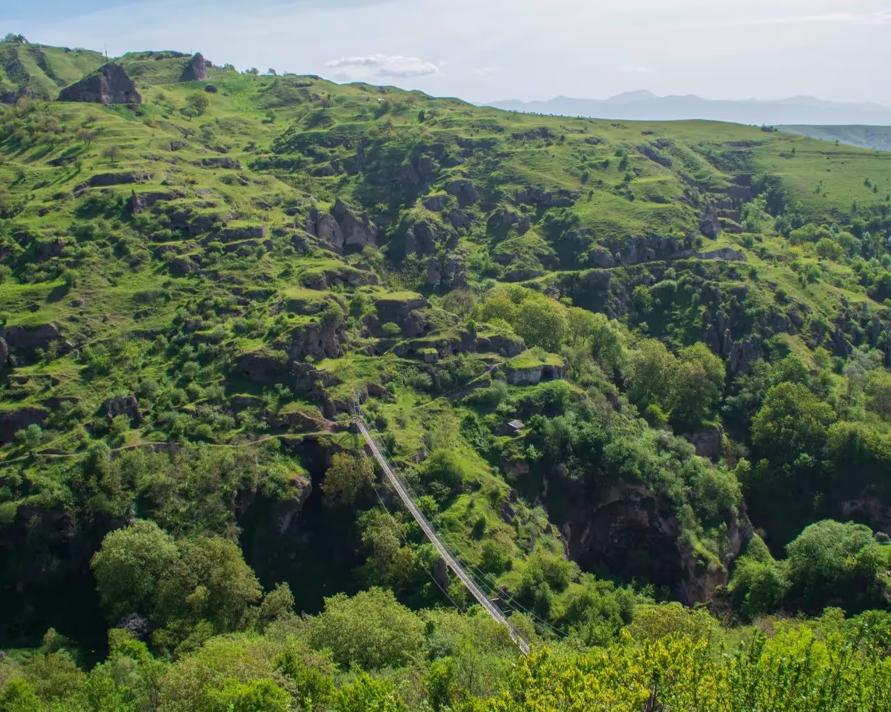 Lush green hills and a famous swinging bridge in Khndzoresk, Armenia.