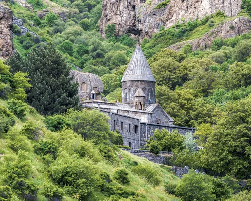 The medieval Geghard Monastery in Armenia, surrounded by lush green hills and carved into rocky cliffs.