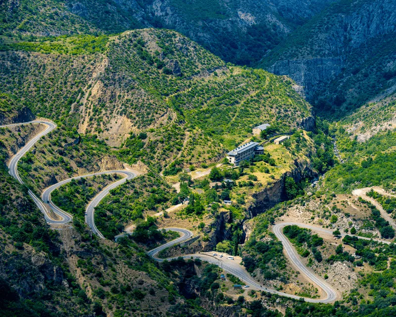 Winding mountain road in Armenia with scenic green hills and a deep gorge in the background.