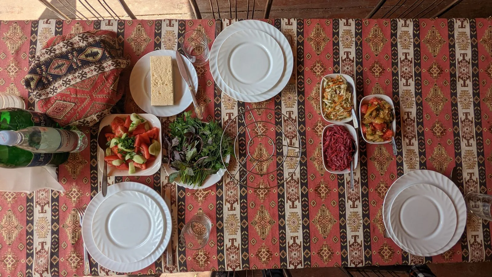 Traditional Armenian meal setup with fresh vegetables, herbs, cheese, and bottled water on an ornate tablecloth.