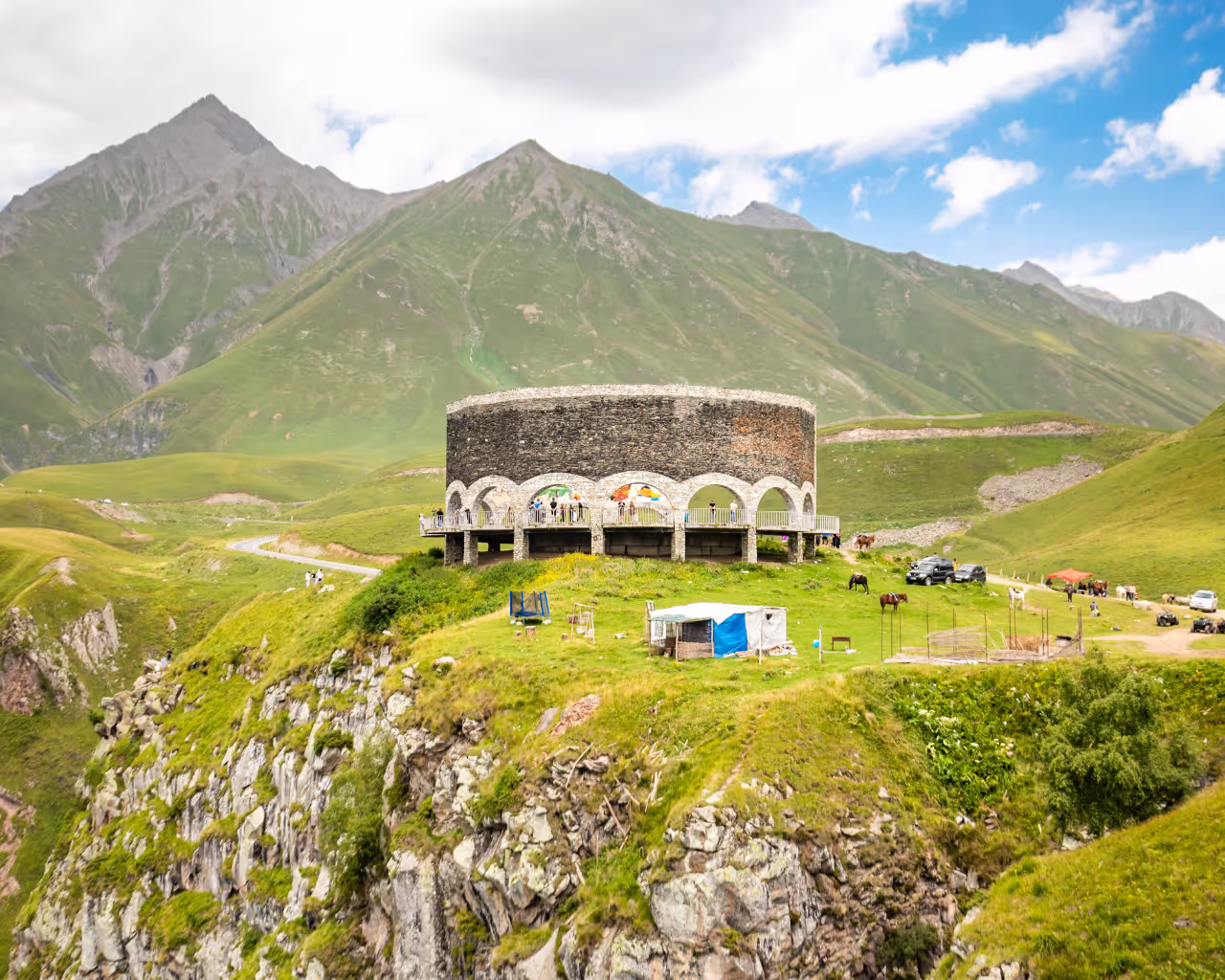 Panoramic view of Gudauri viewpoint in Georgia, a semi-circular monument overlooking lush mountains.