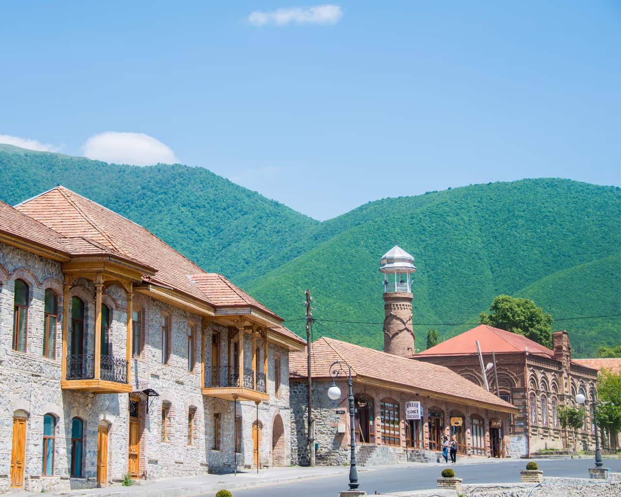 Sheki, Azerbaijan cityscape with historic stone buildings and lush green mountains in the background.