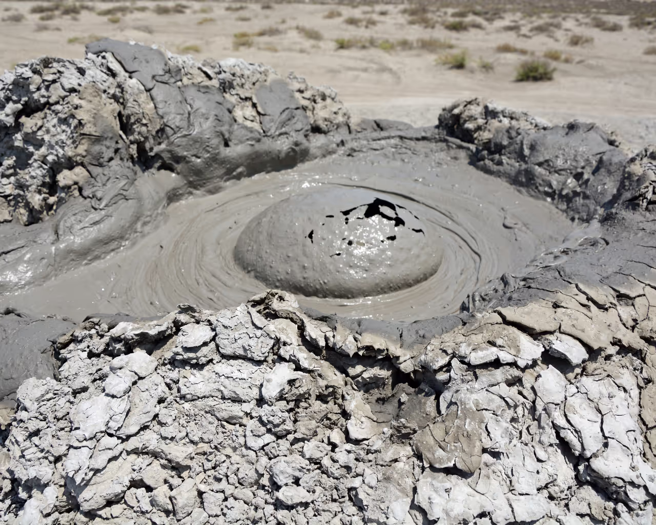 Bubbling mud volcano in Azerbaijan, natural geological formation with thick, gray mud erupting from the cracked surface.