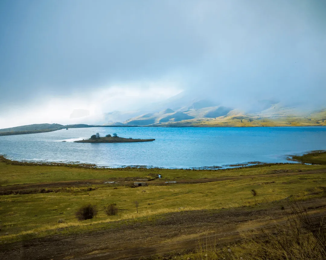 Serene mountain lake in Nakhchivan, Azerbaijan, with a small island and misty hills in the background.