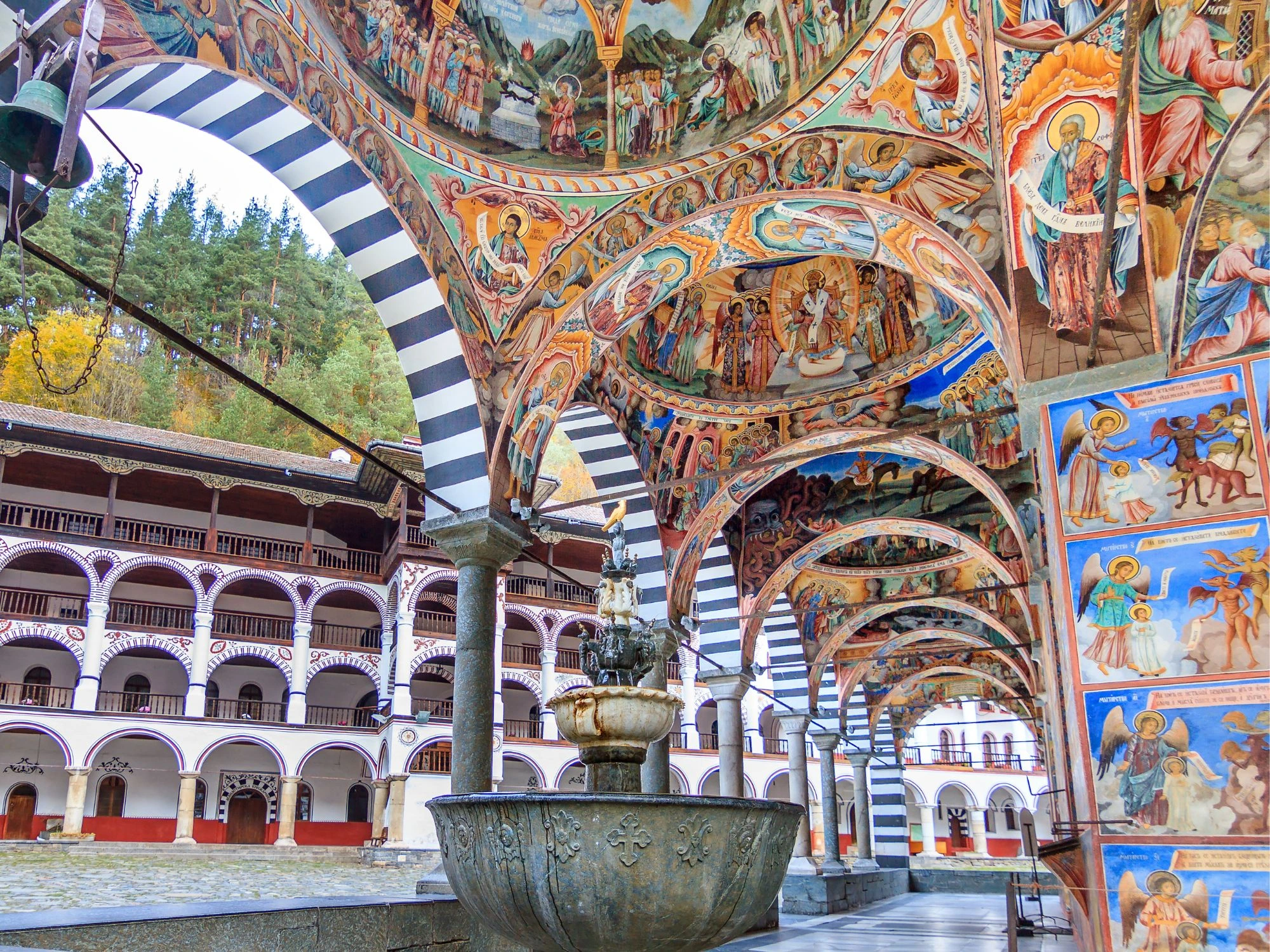 Bulgaria–Rila Monastery arcade with striped arches and colorful religious murals.