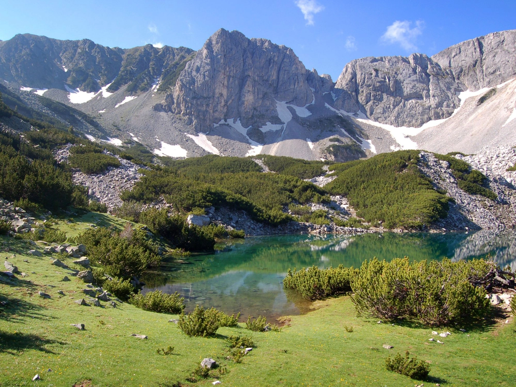 A turquoise glacial lake in Pirin Mountain, Bulgaria, surrounded by alpine greenery and rugged peaks.
