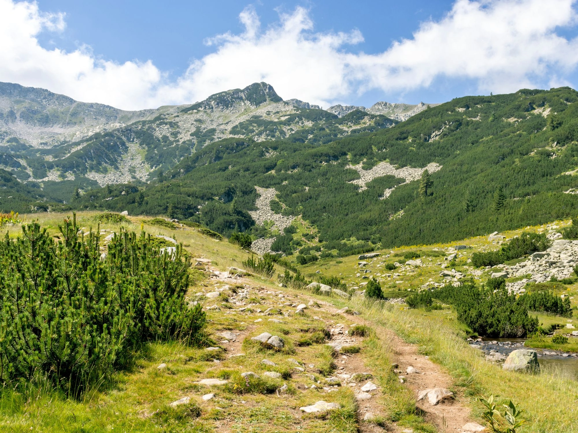 Stacked stone cairn on a rocky ridge in Pirin Mountain, Bulgaria, marking a high-altitude trail.