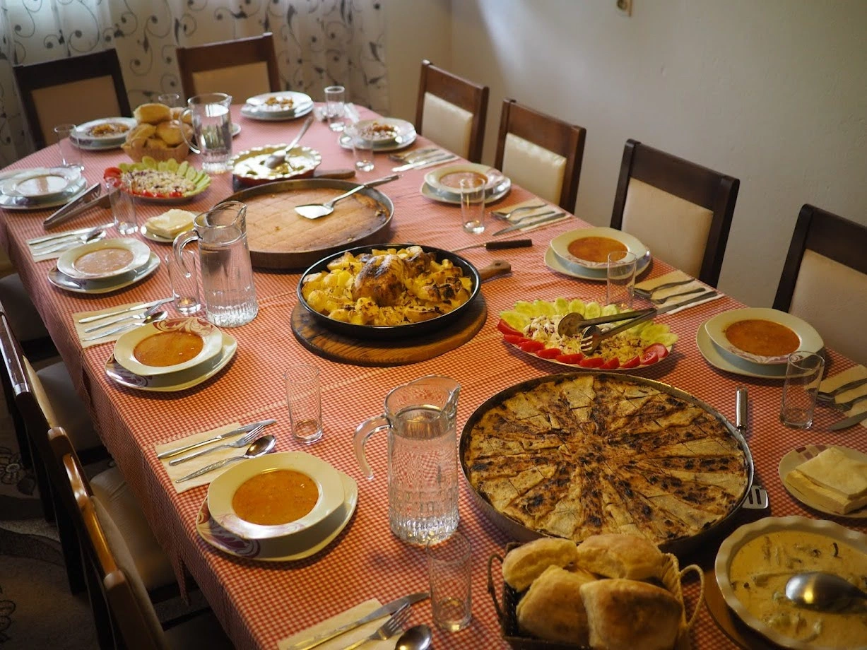 A table filled with homemade dishes, including traditional pies, soups, fresh bread, and salad, set for a meal.