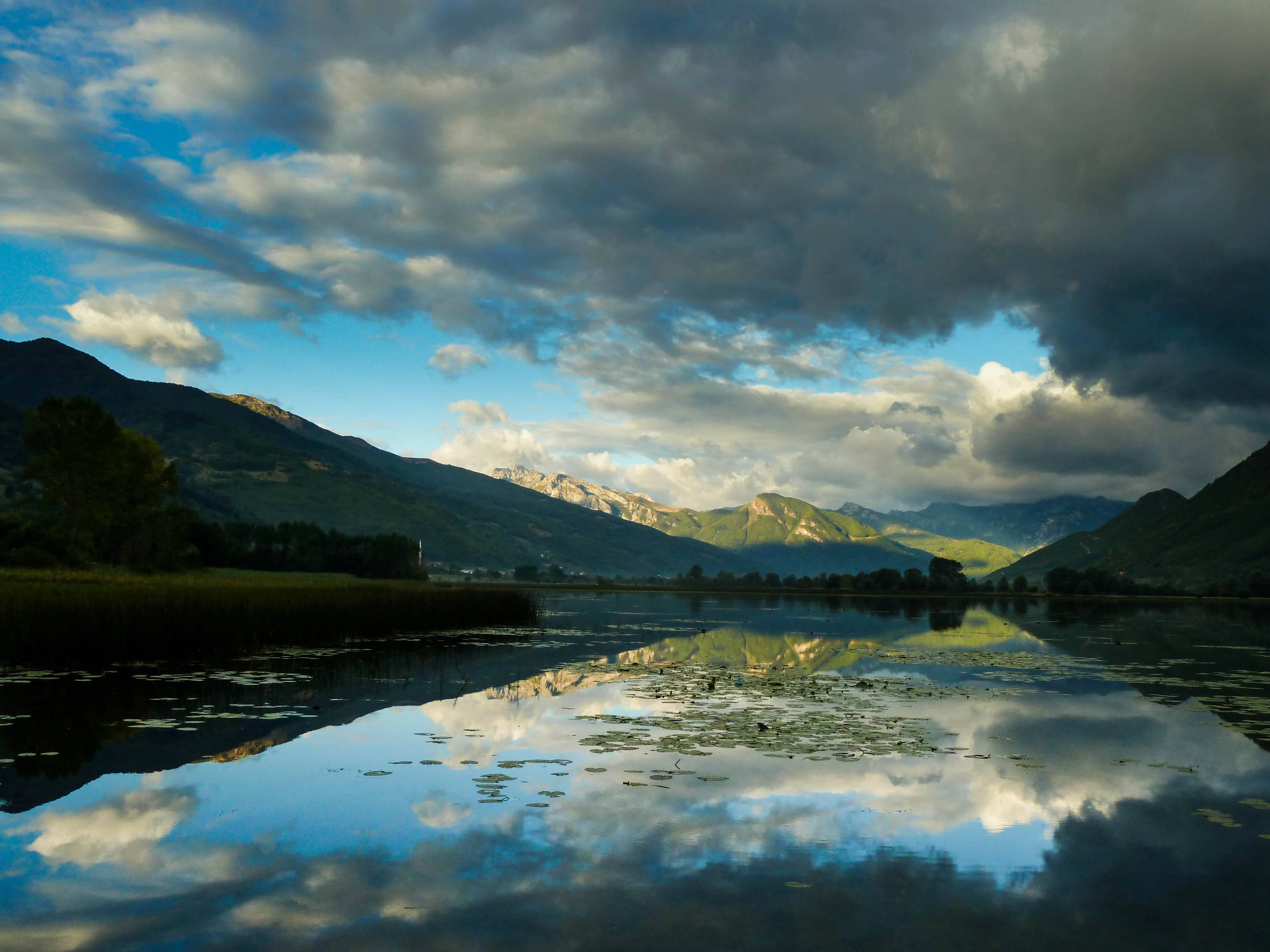 A tranquil lake reflecting dramatic clouds and mountains in the Albanian Alps.