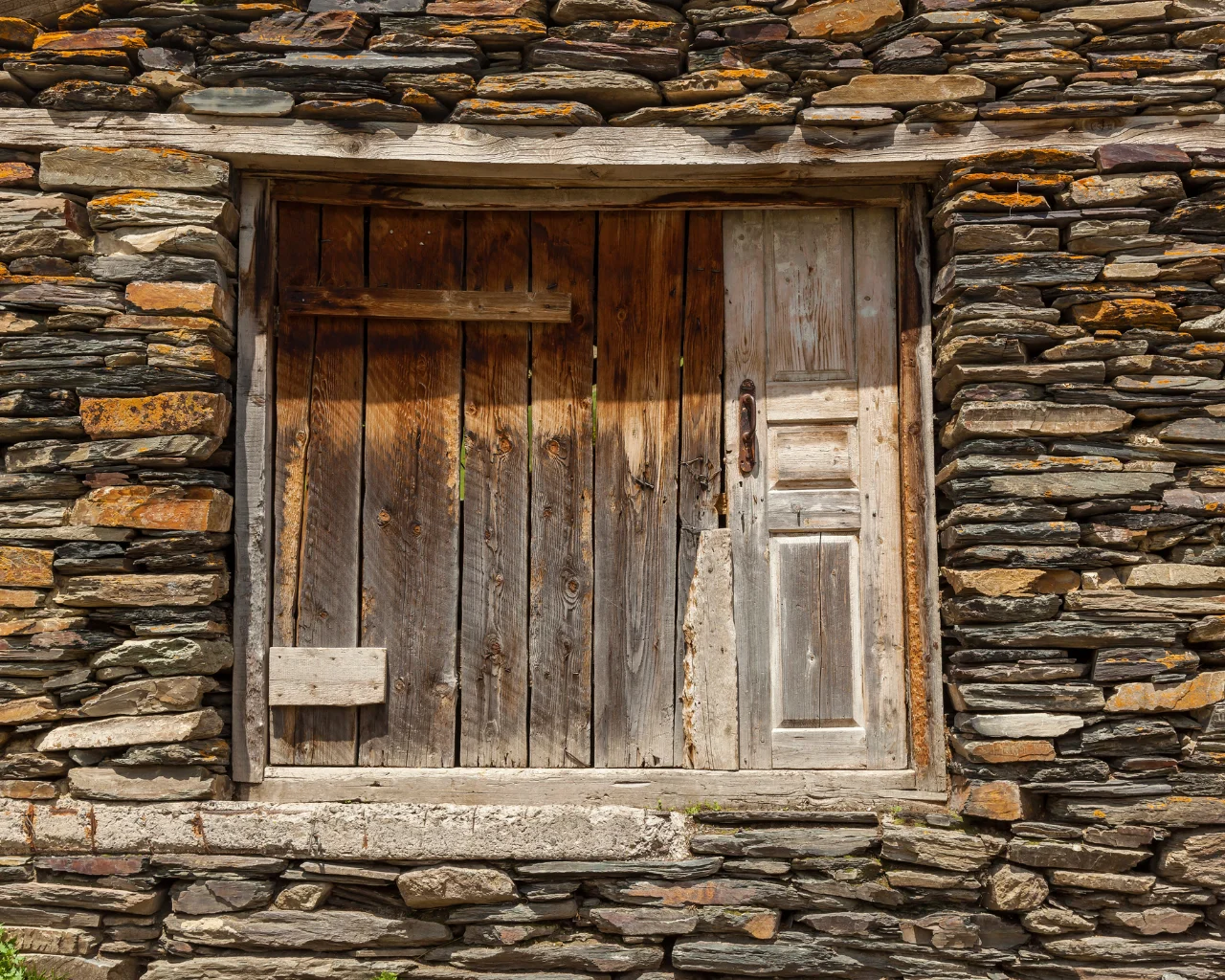 A weathered wooden door set in a stone house in Svaneti, Georgia, showcasing traditional mountain architecture.