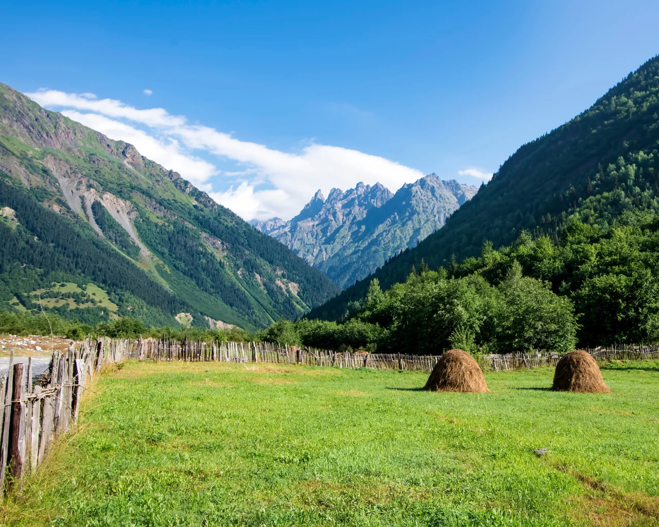 A fenced pasture with haystacks, surrounded by towering green mountains in Svaneti, Georgia.