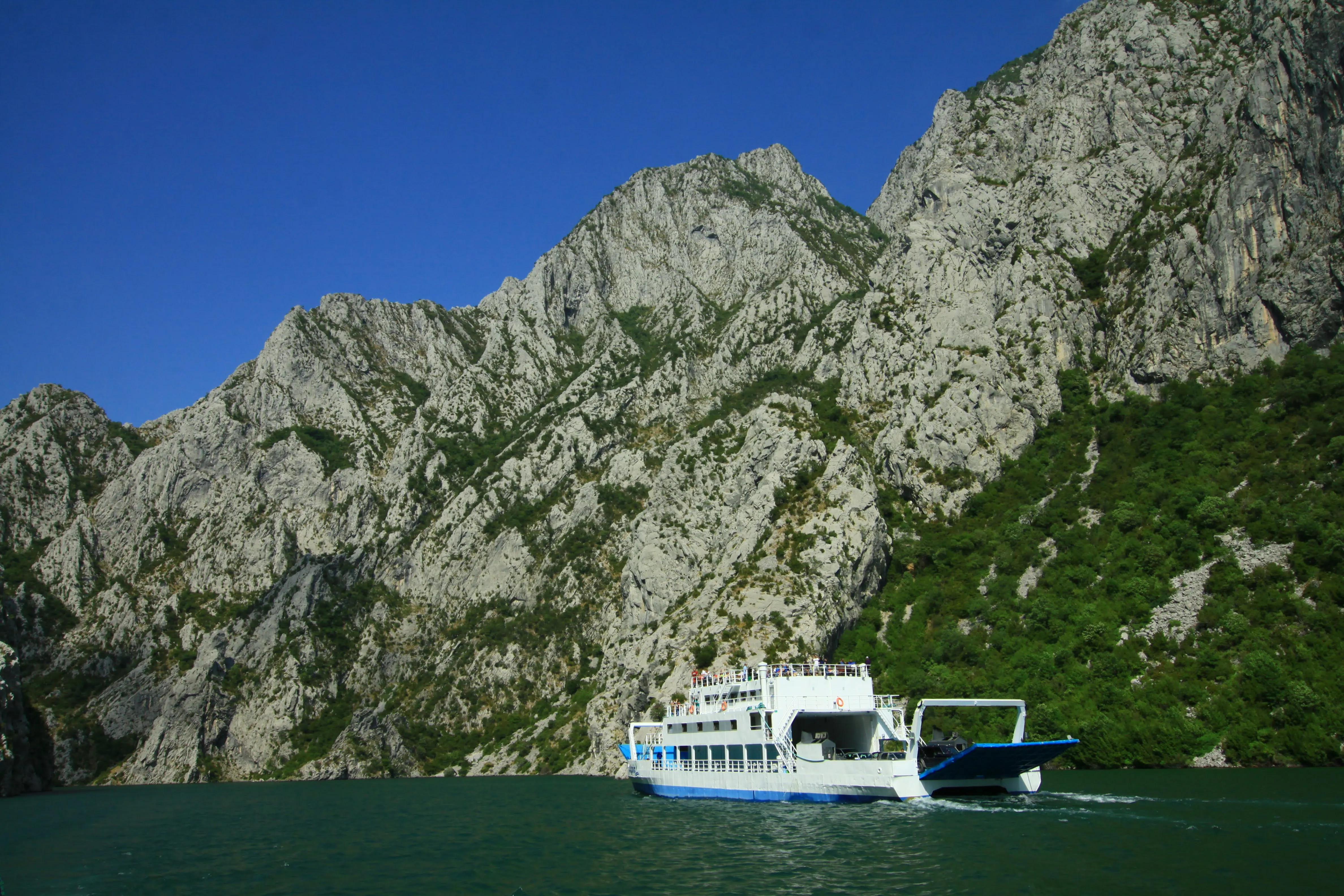 A ferry crossing Koman Lake, Albania, with steep limestone cliffs rising above the turquoise waters under a clear sky