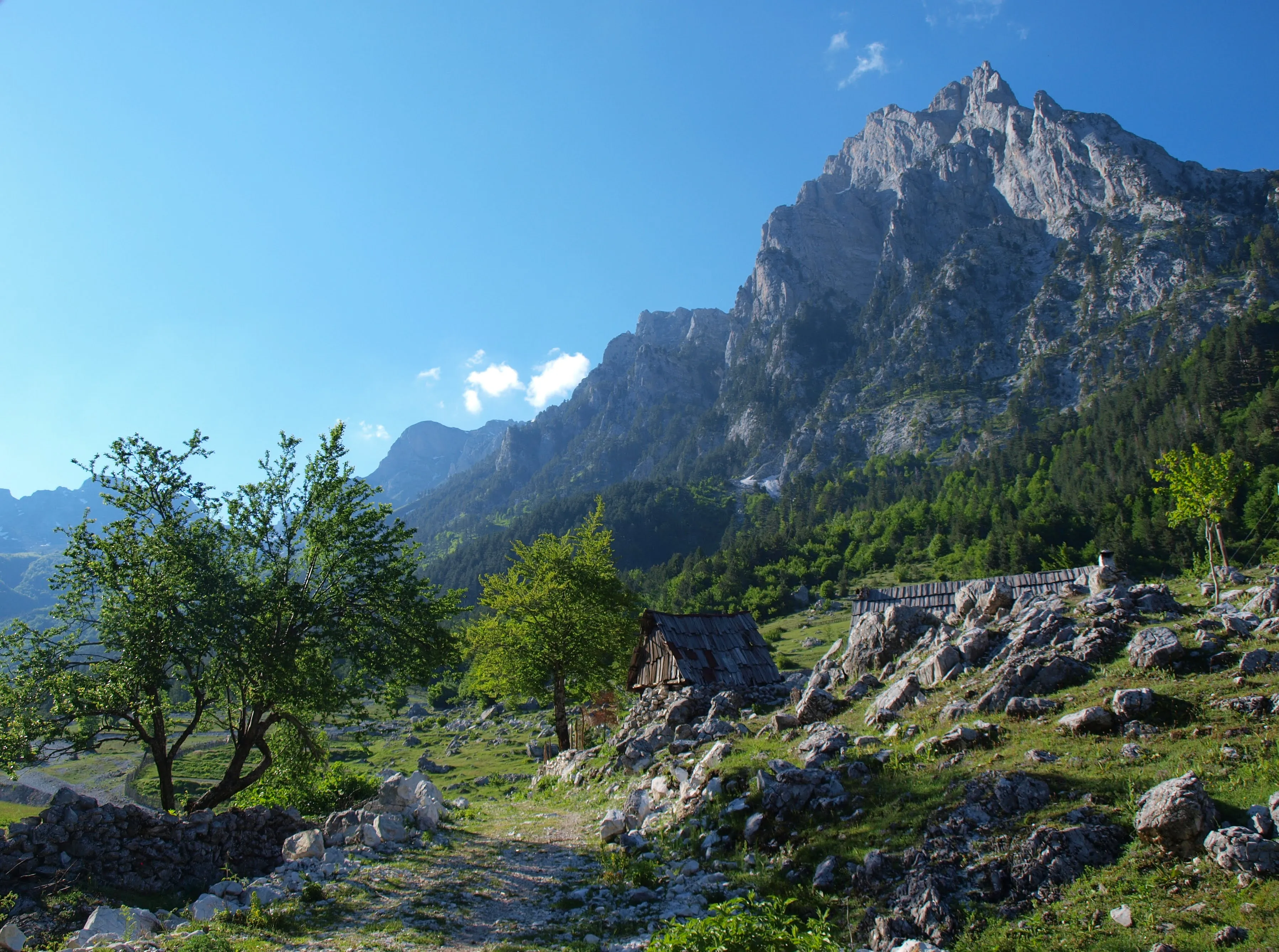 Rugged mountain landscape in Valbona, Albania, with scattered wooden huts and lush greenery under a clear blue sky