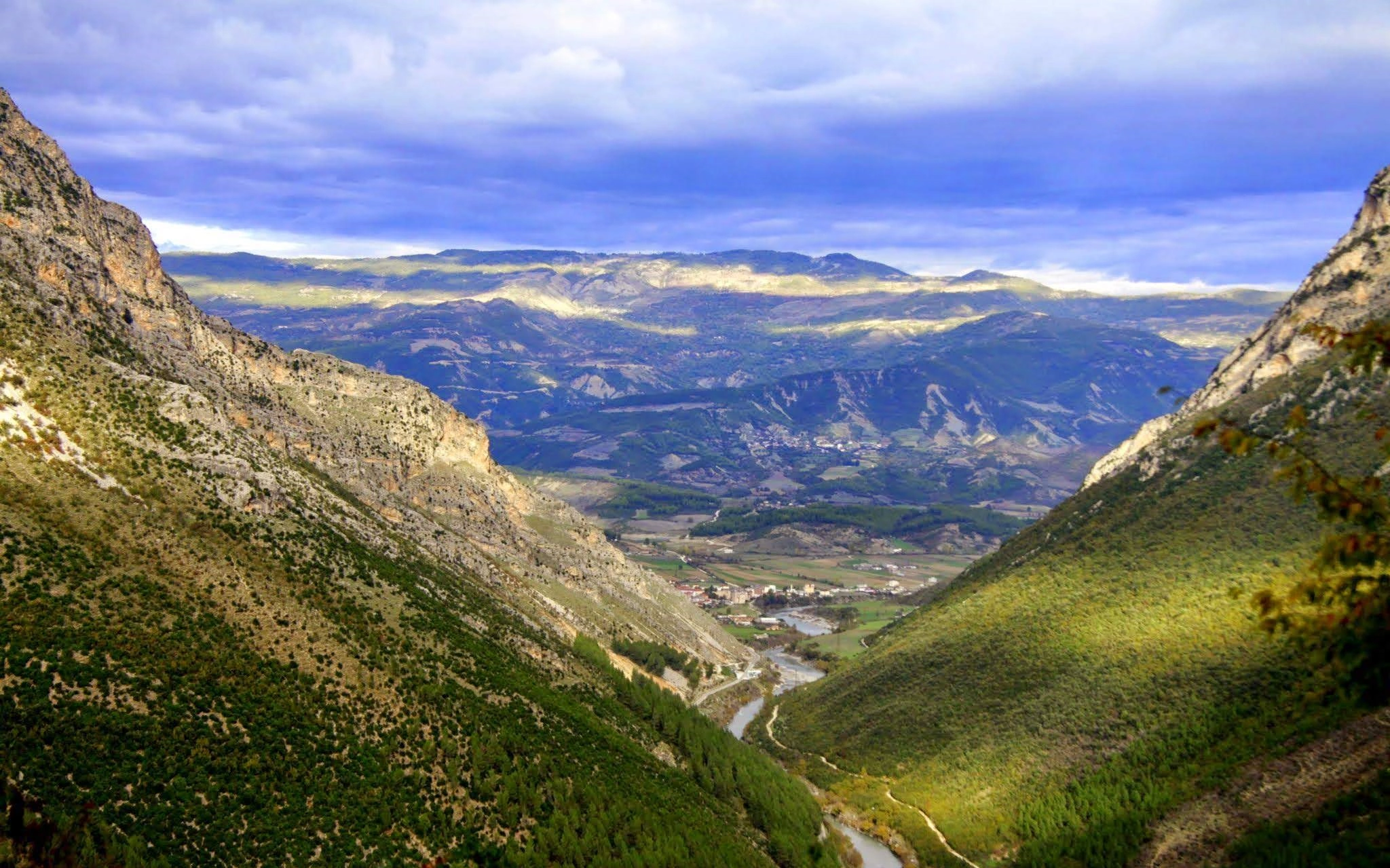 A valley with a winding river, framed by rugged mountains under a dramatic cloudy sky.