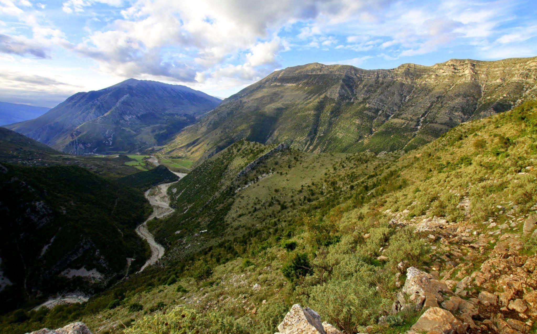 A panoramic view of a deep valley with a winding river and distant mountains under a partly cloudy sky.