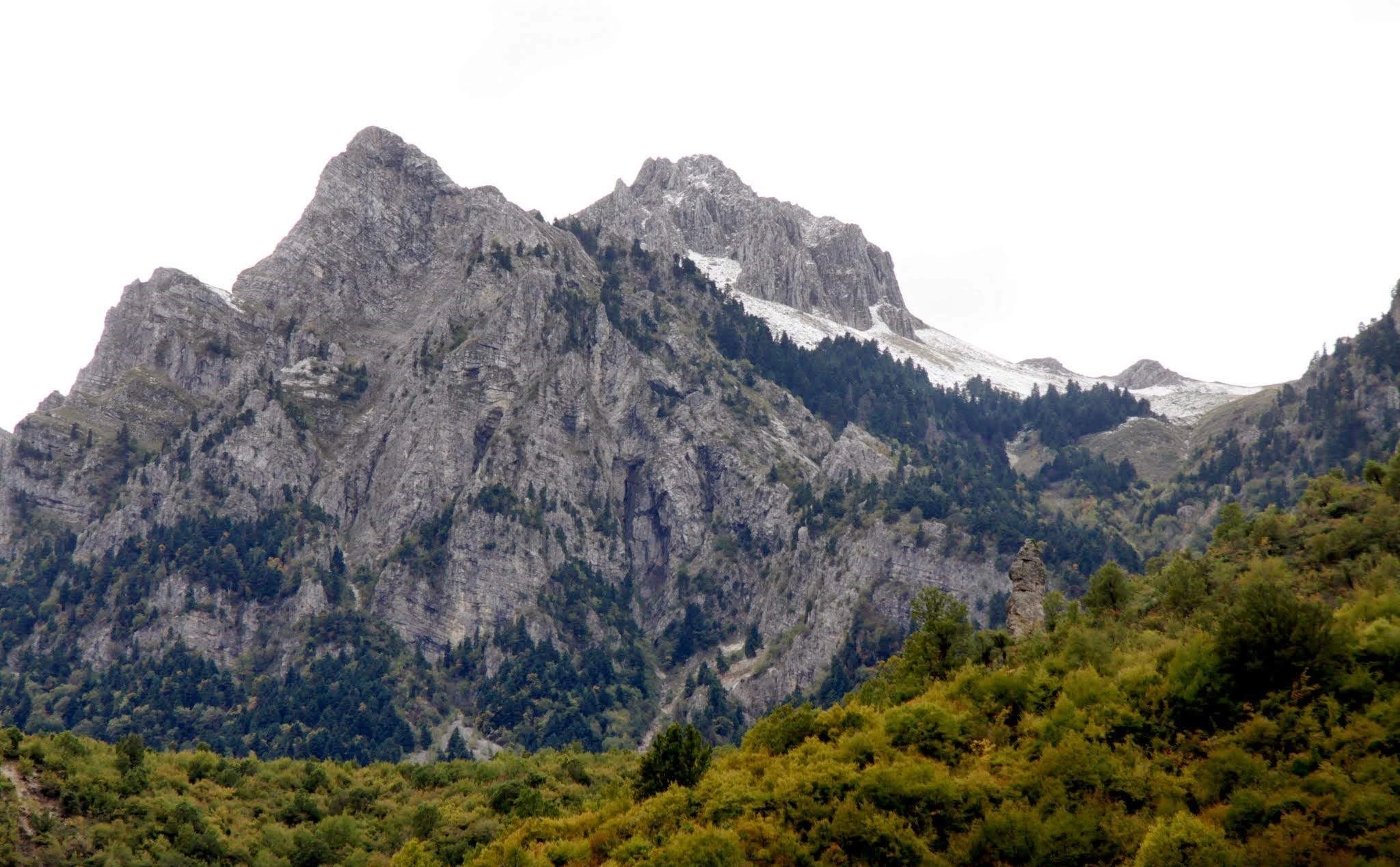 Jagged mountain peaks with steep rocky slopes and patches of greenery beneath a cloudy sky.