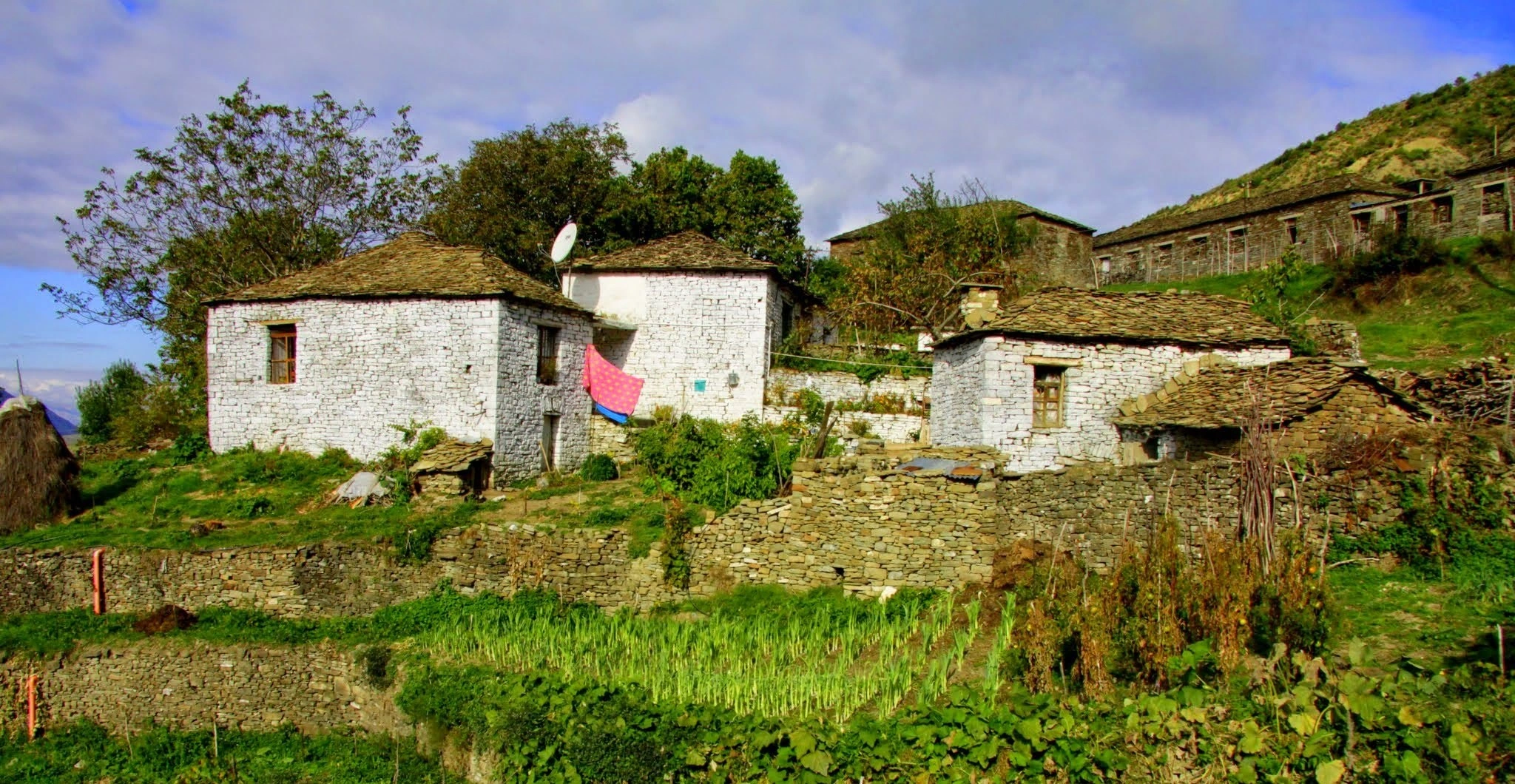 Whitewashed stone houses with wooden roofs in a hillside village, with a pink cloth hanging outside.