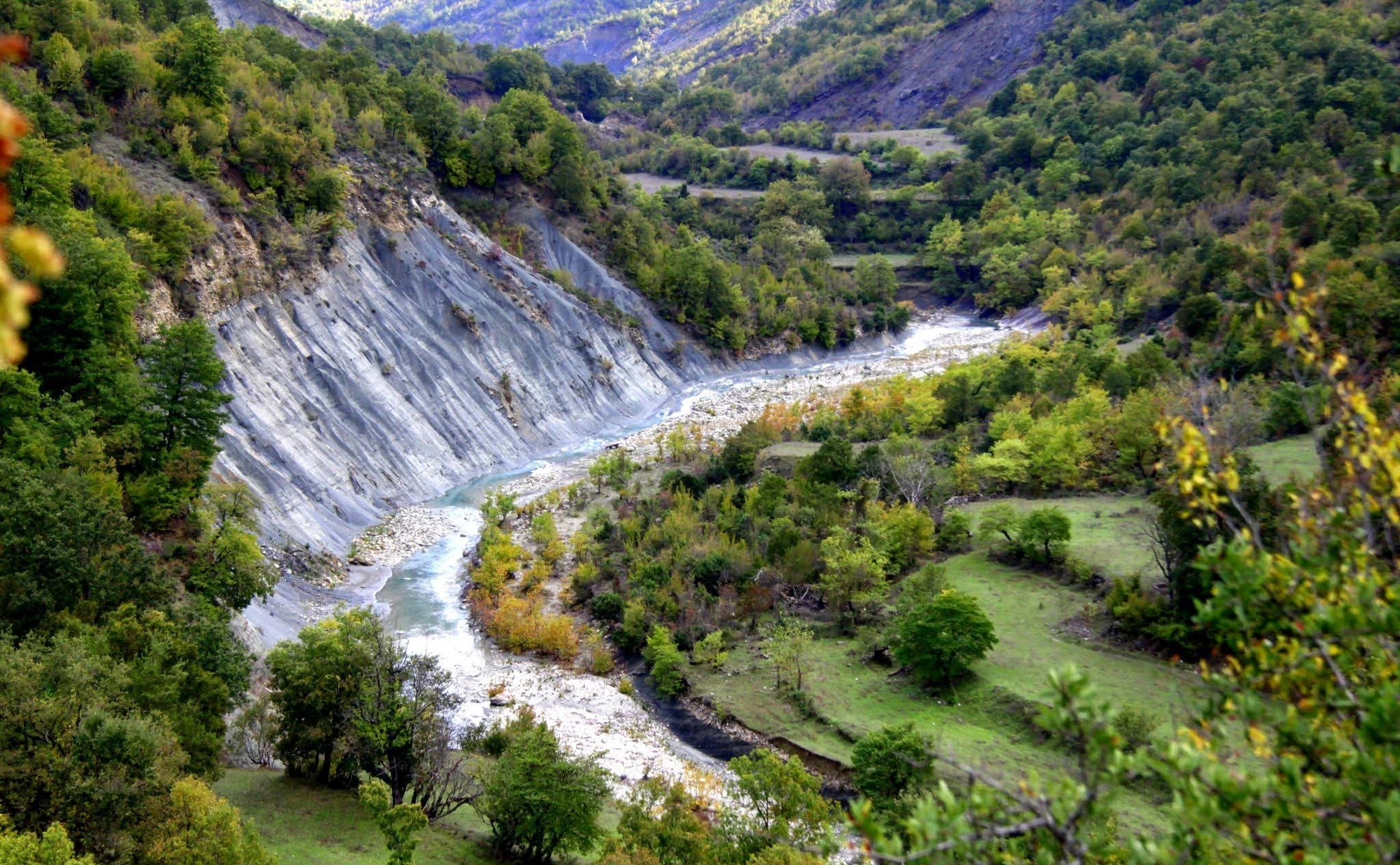 A winding river flows through a lush valley, carving steep rock formations in the Albanian mountains.