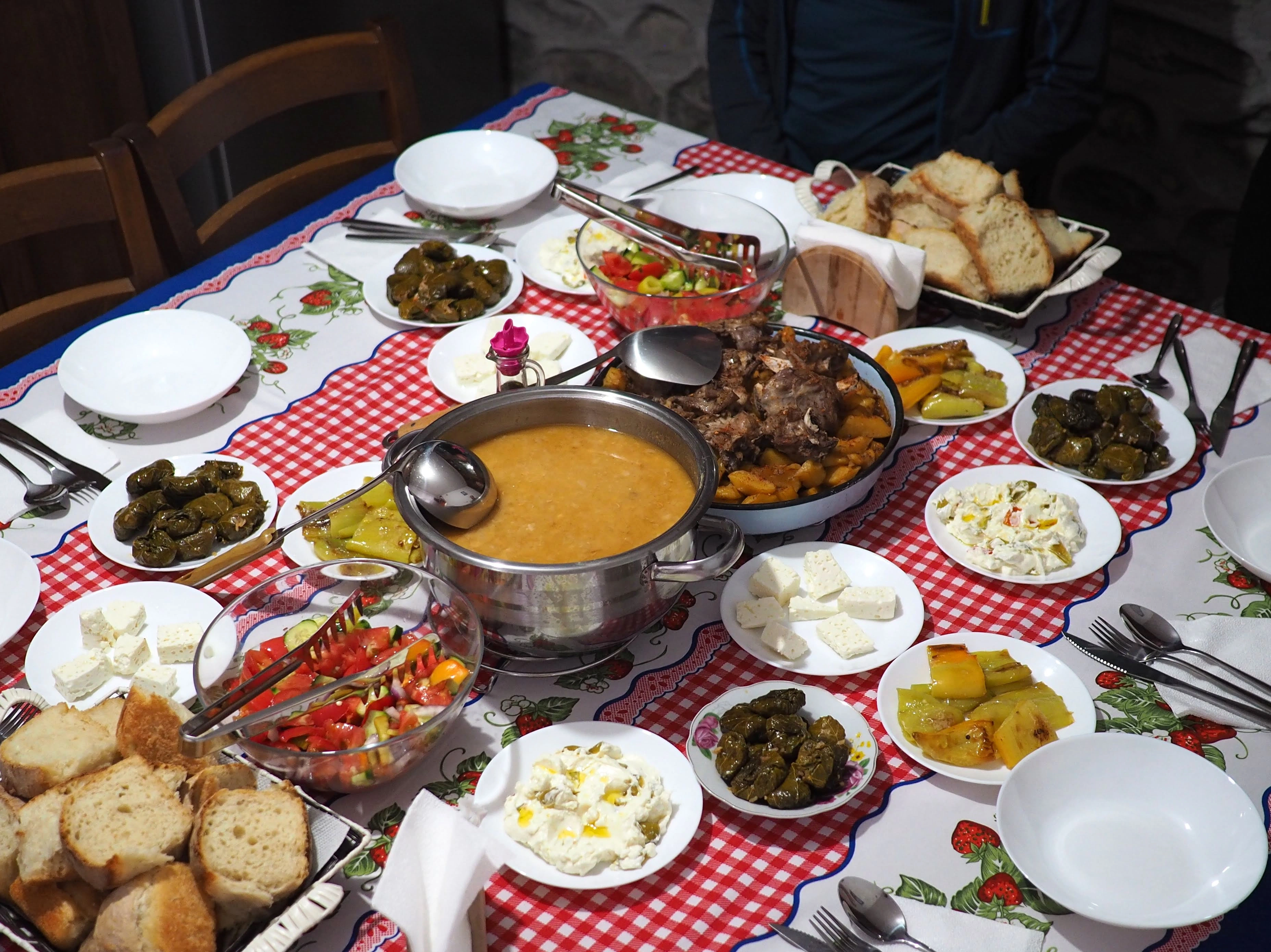 A table with a red-checkered cloth is filled with local dishes, fresh cheese, bread, and stuffed peppers