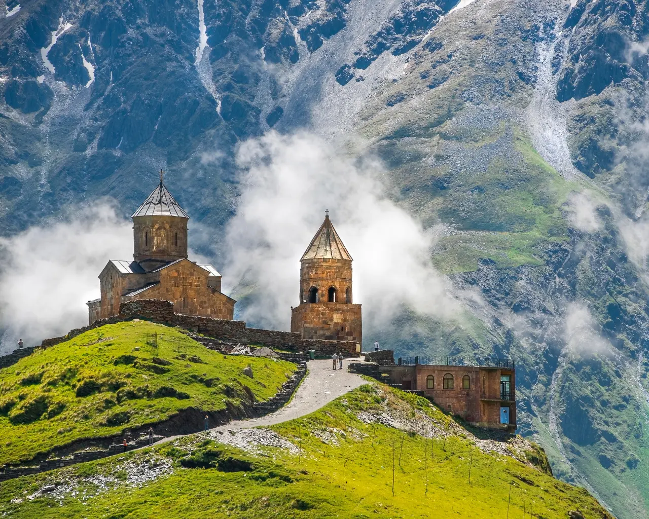 Gergeti Trinity Church - Ancient stone church atop a green hill, surrounded by misty mountains in Kazbegi, Georgia.