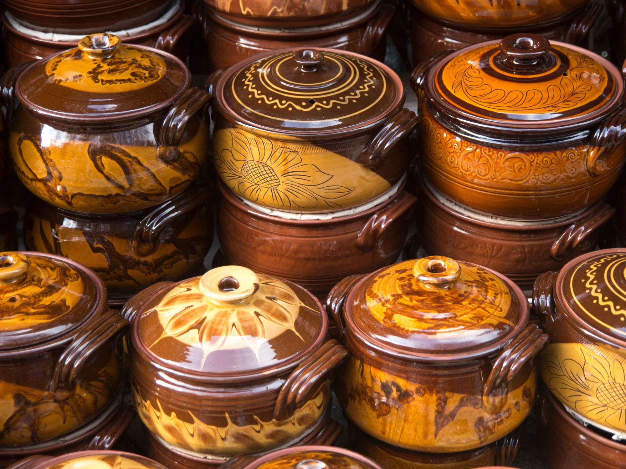 Handmade brown ceramic pots with intricate patterns stacked at a market, showcasing Bulgarian pottery craftsmanship.