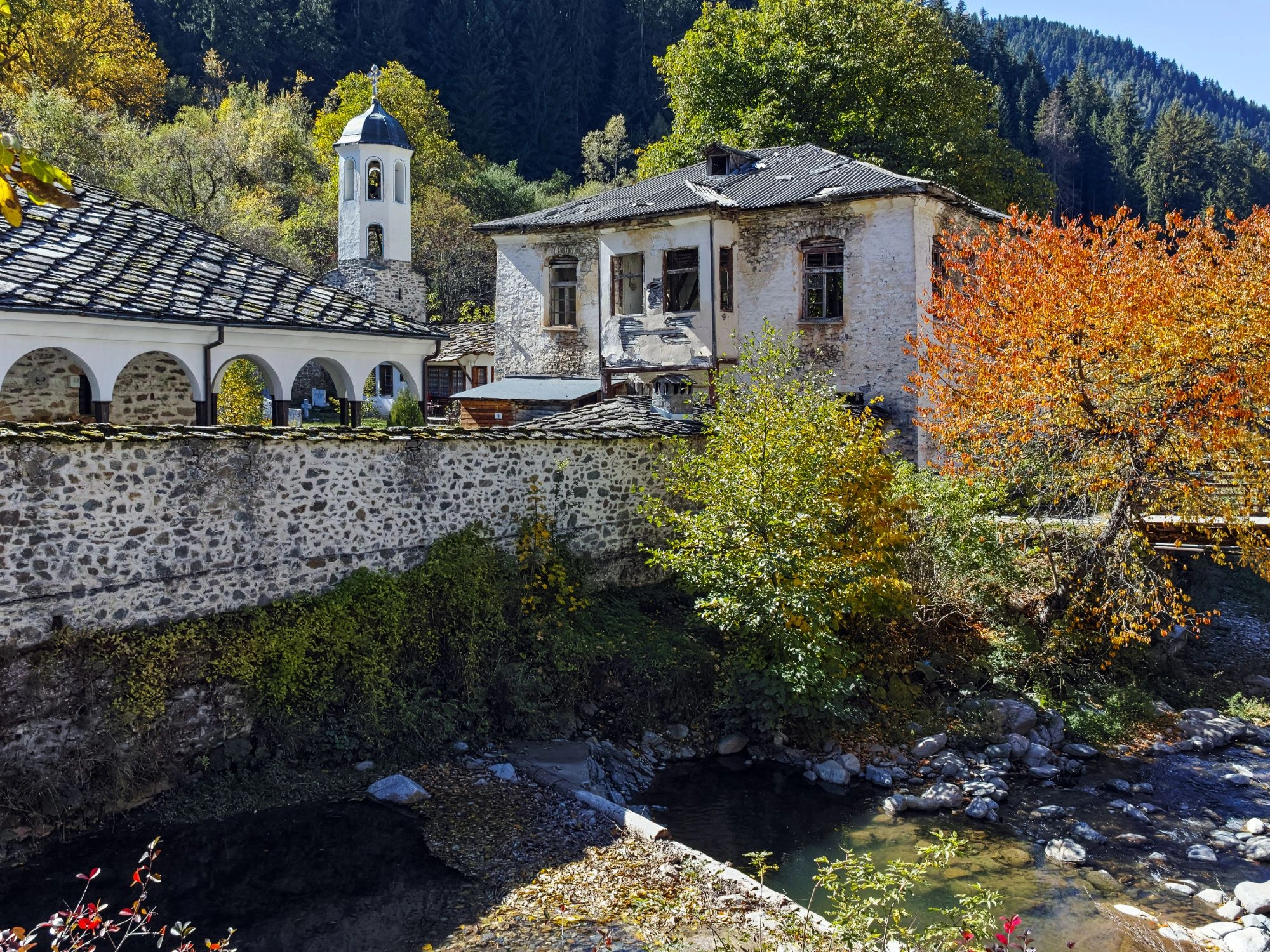 Rhodope Mountains, Bulgaria - A historic stone monastery with a bell tower, surrounded by autumn foliage in the Rhodope Mountains.