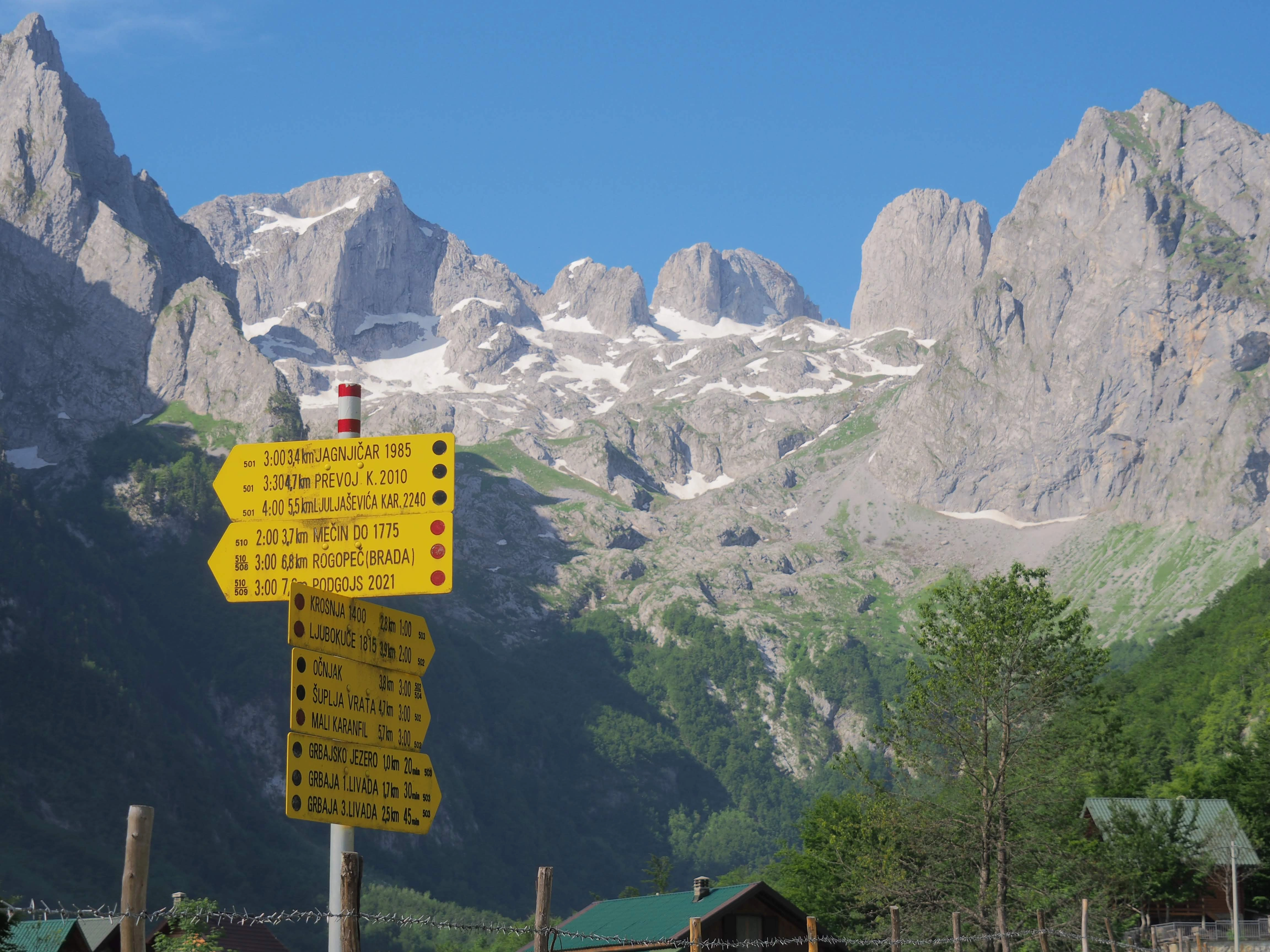 Yellow hiking trail signs in Theth, Albania with majestic Albanian Alps in summer.