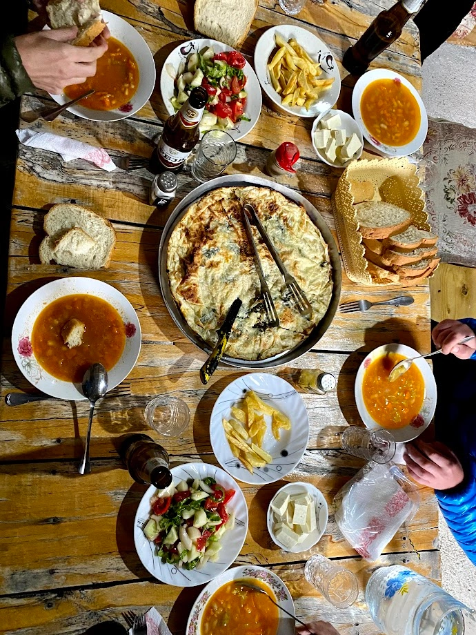 A traditional meal spread with soup, salad, bread, and a large flaky pie on a wooden table.