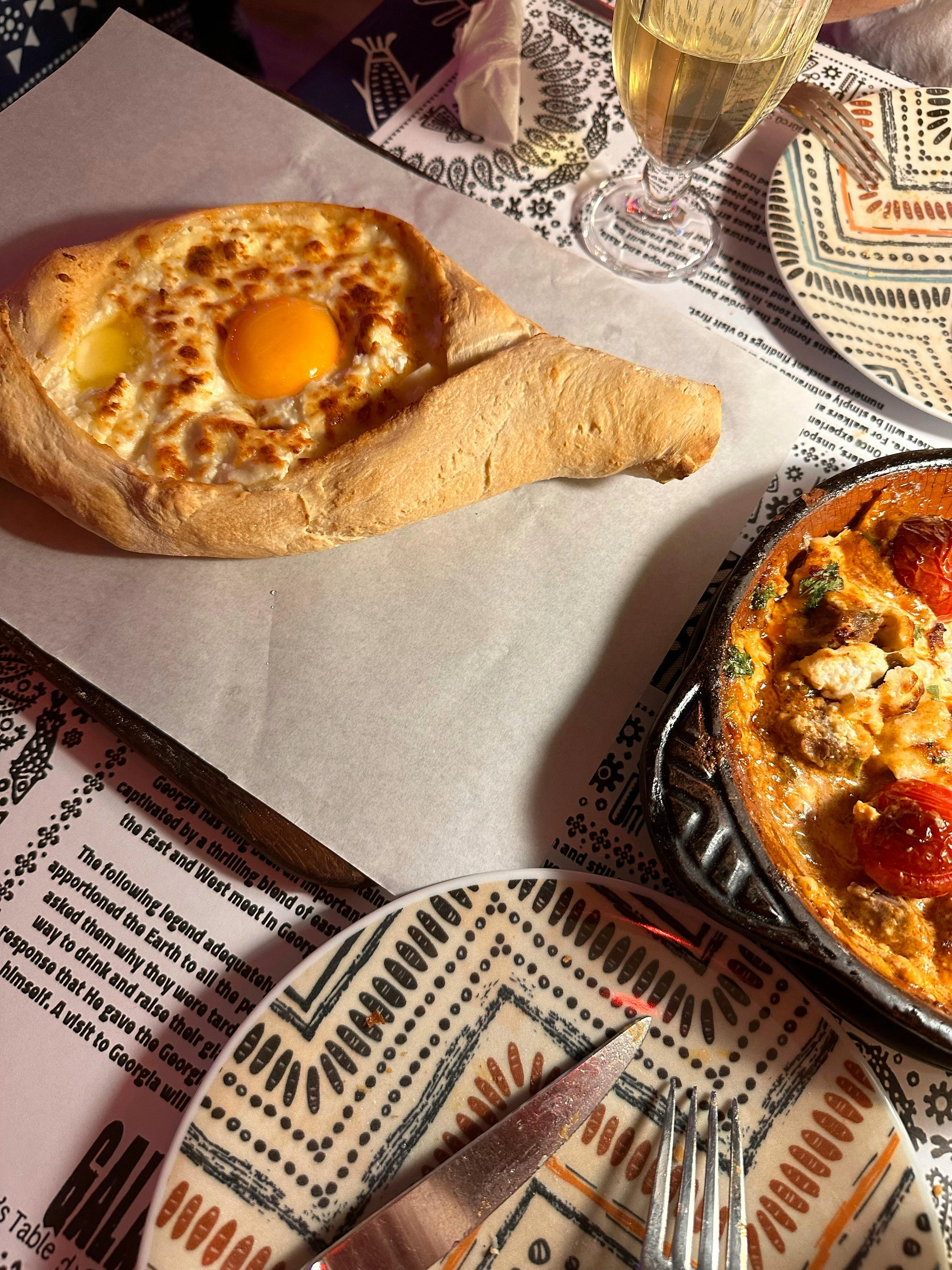 A freshly baked Adjarian khachapuri with melted cheese and egg, served with traditional Georgian dishes and wine.