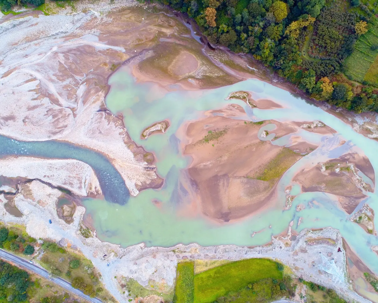 Aerial view of a winding river in Adjaristskali, Georgia, with sandbanks and turquoise water cutting through green hills.