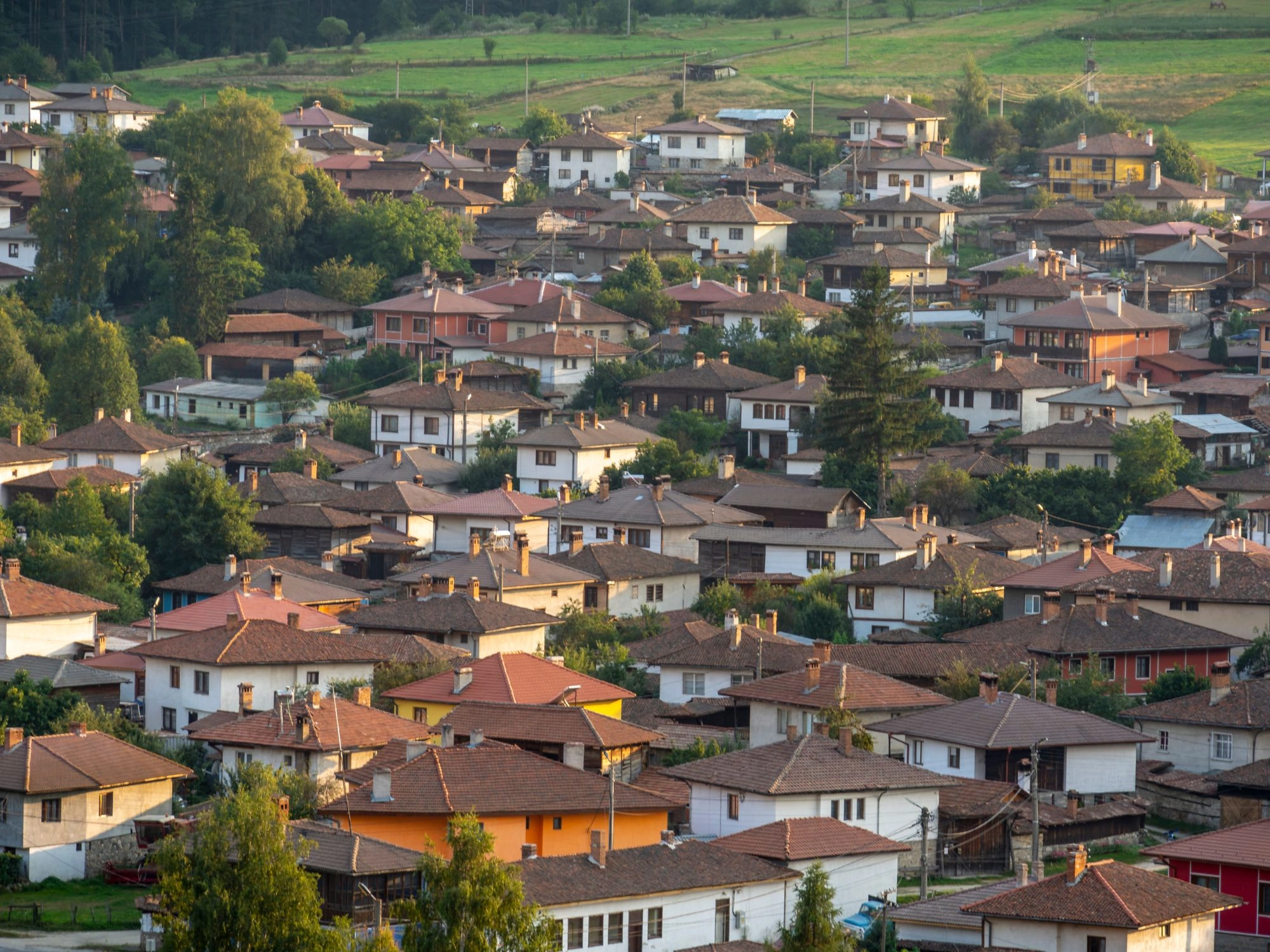 Koprivshtitsa, Bulgaria – A village with red-tiled roofs and colorful houses, nestled in a green valley with rolling hills.