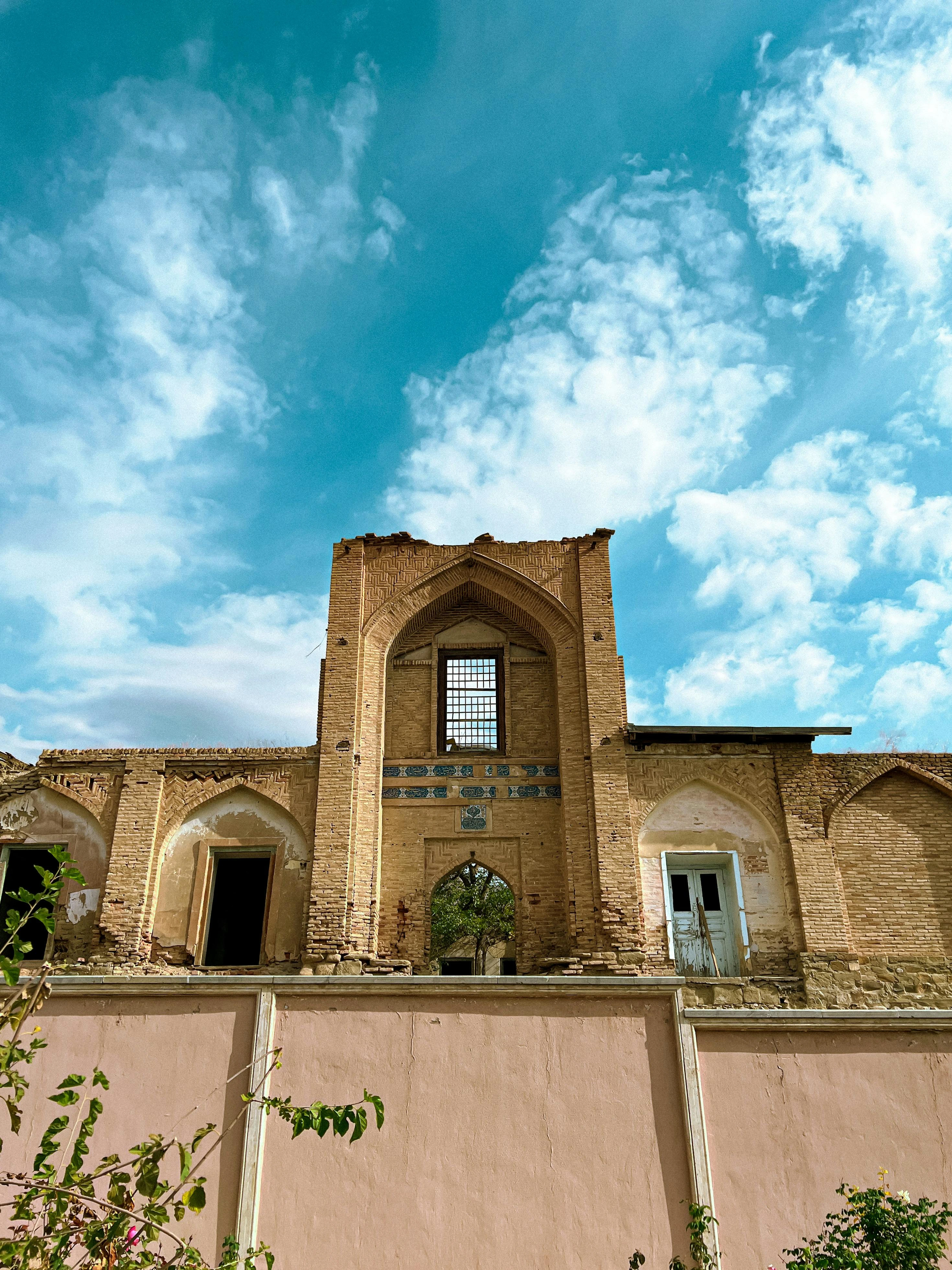 Partially restored historic building in Azerbaijan, with intricate brickwork and blue tile accents against a cloudy sky.
