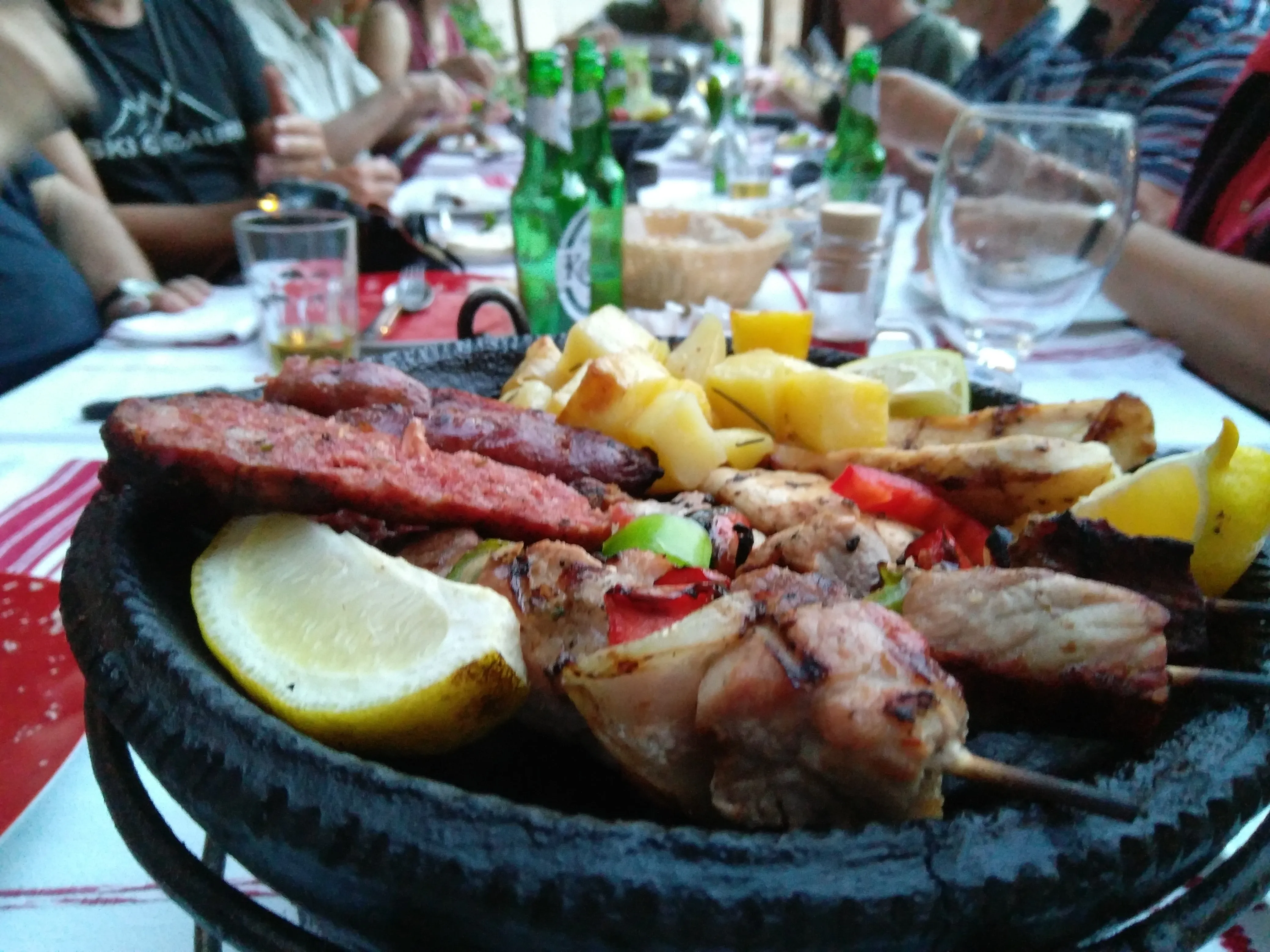 A sizzling platter of grilled meat, sausages, and roasted potatoes served at an outdoor Albanian feast.