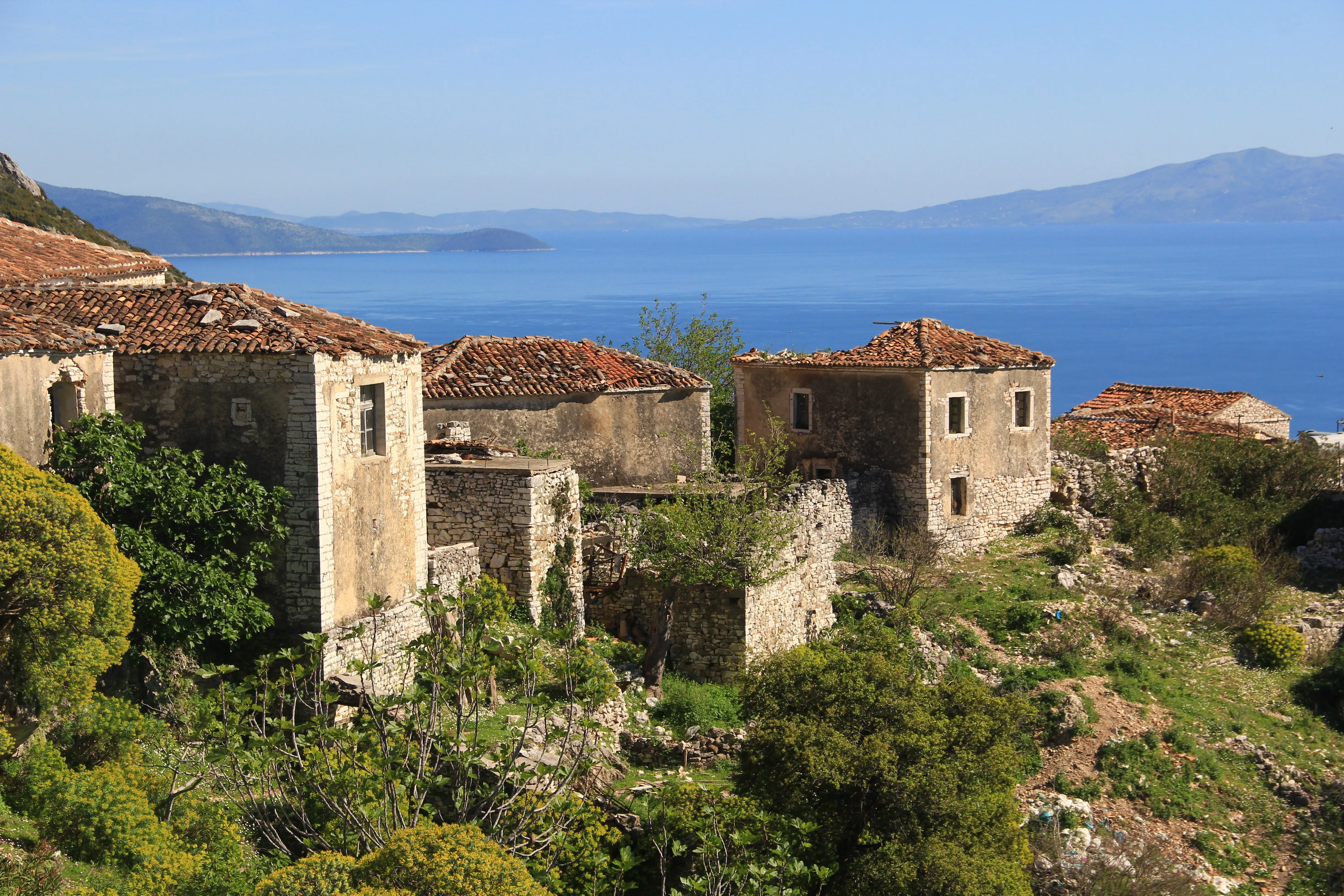 Abandoned stone houses with terracotta roofs, overlooking the Ionian Sea from a hilltop village in Albania.