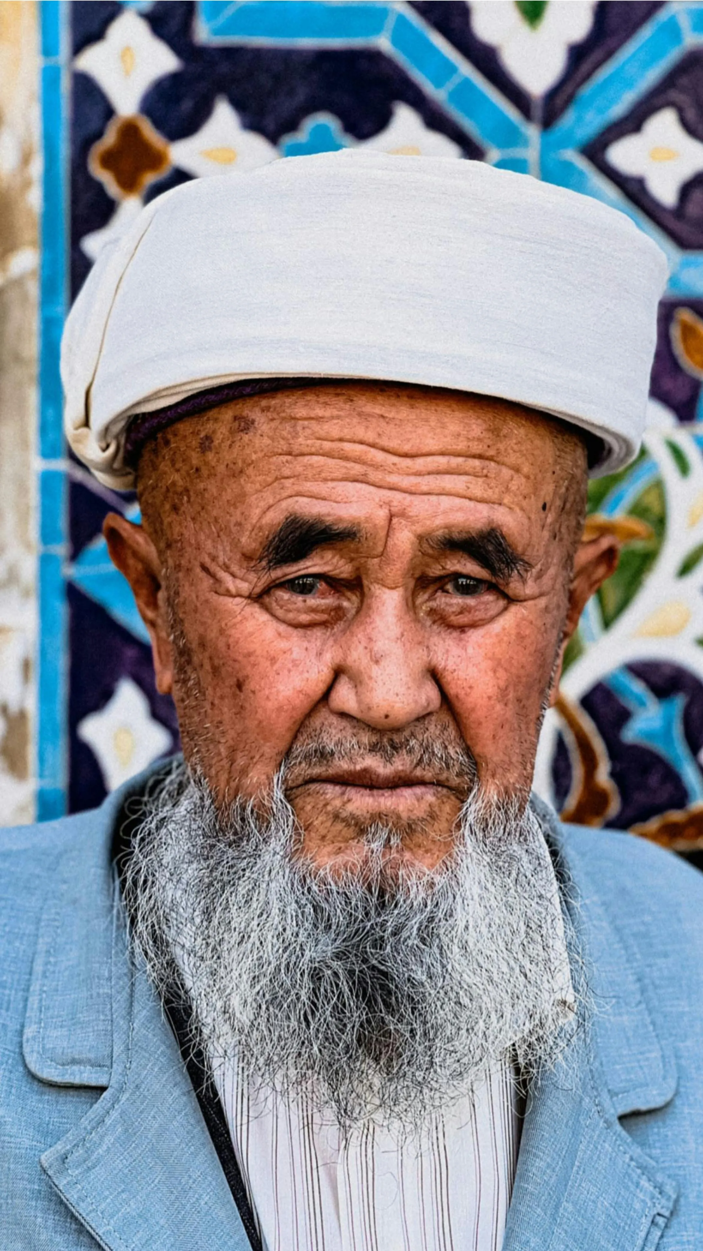 Portrait of an elderly Uzbek man wearing a white turban with a traditional tiled backdrop.
