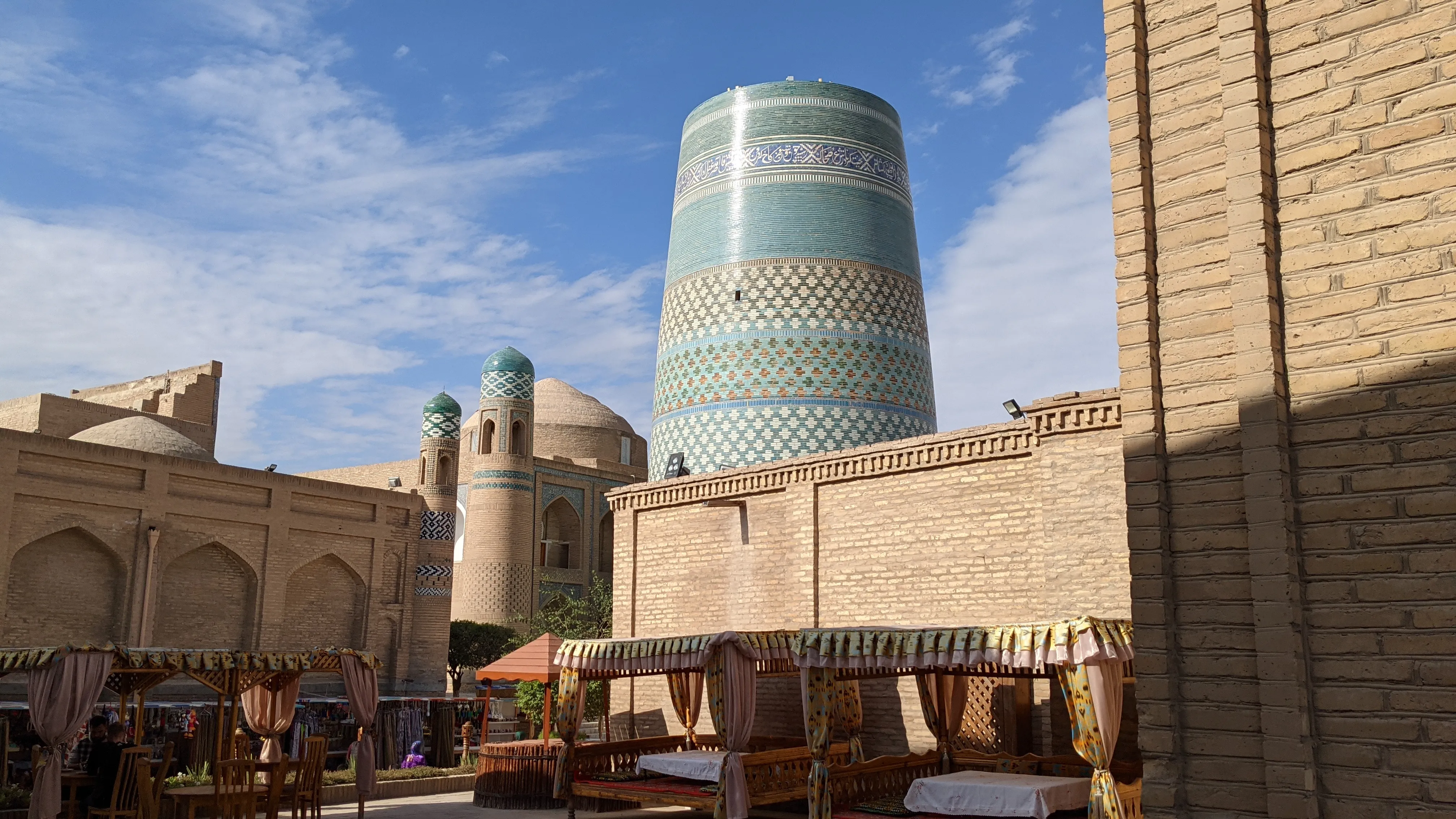 Khiva, Uzbekistan: The striking turquoise Kalta Minor Minaret stands in Khiva’s historic cityscape under a blue sky.