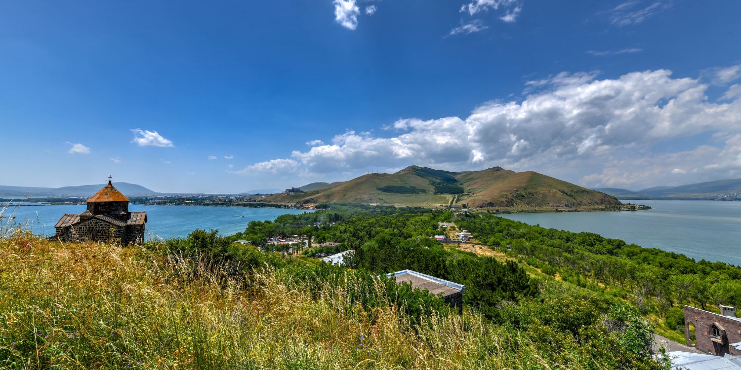 Lake Sevan scenic view with Sevanavank Monastery and green hills under a bright sky.