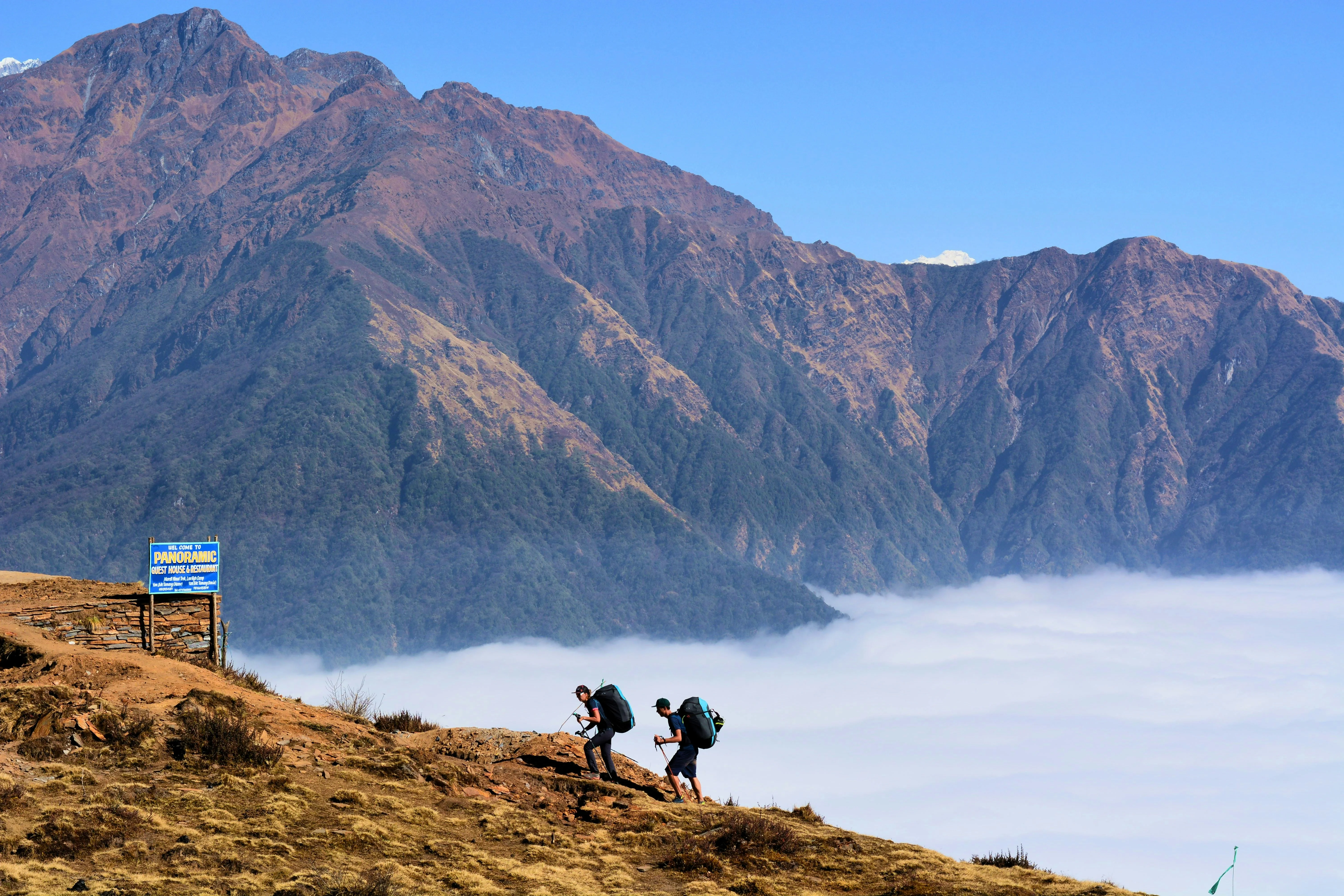 Two hikers trekking above the clouds with dramatic mountain peaks in the distance.