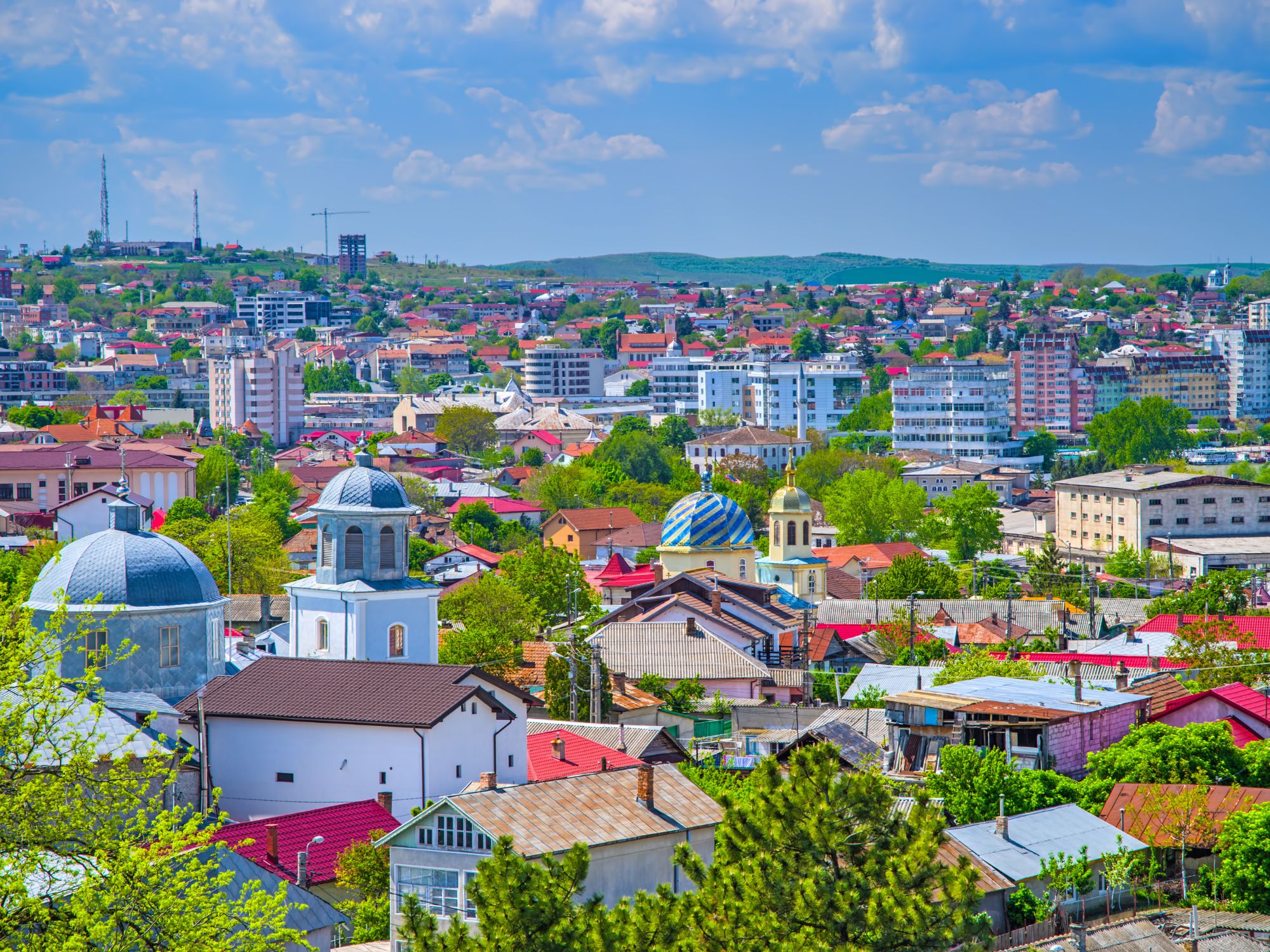 A panoramic view of Tulcea, Romania, showcasing colorful rooftops, churches, and modern buildings under a blue sky.