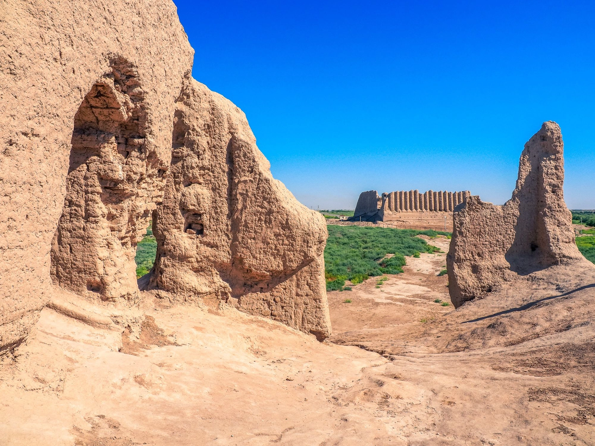 Ancient fortress wall ruins at Kepderihana in Merv, Turkmenistan, framed by desert plants.