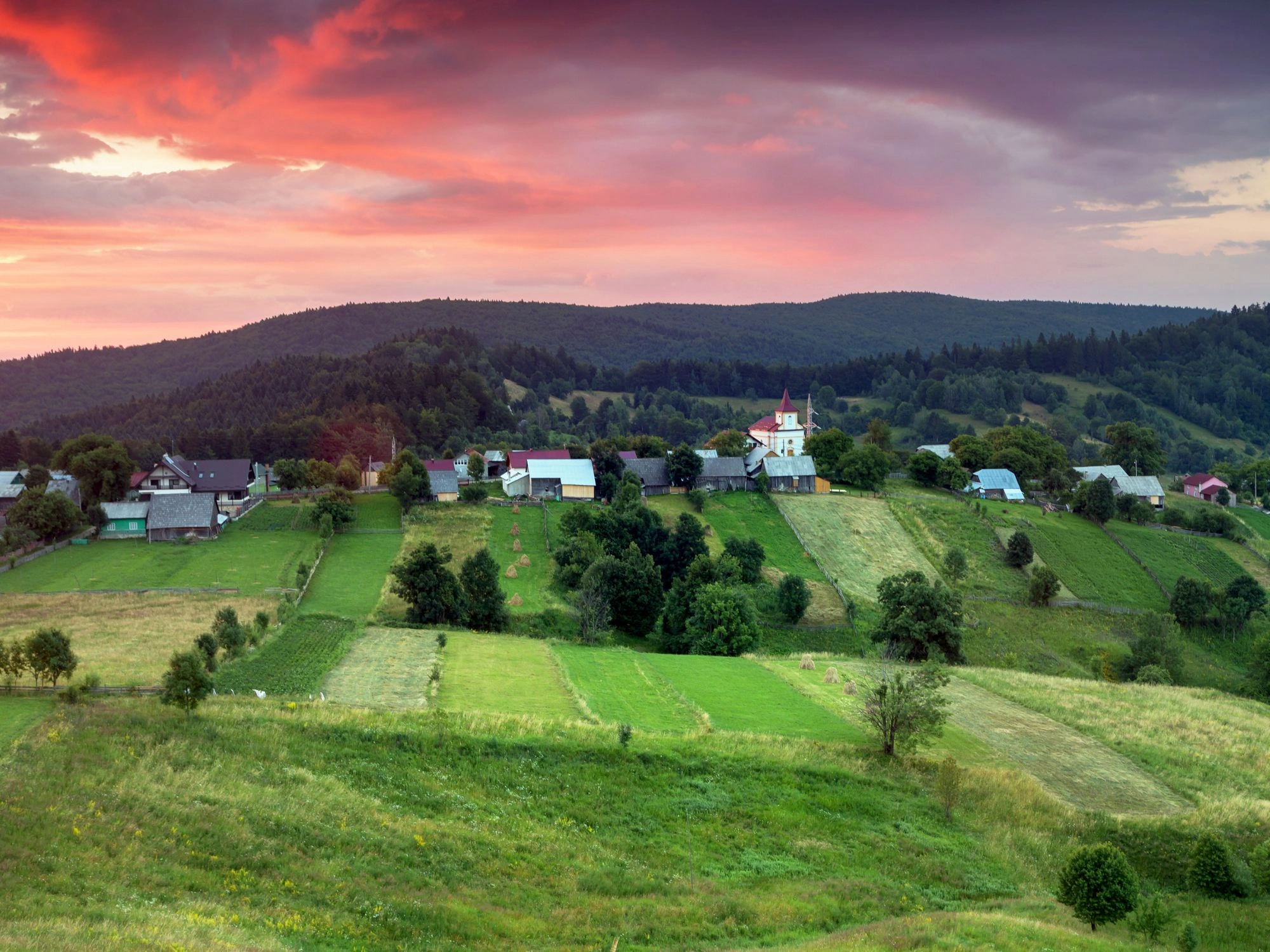 Bucovina countryside with scattered homes and red-roof church at sunset