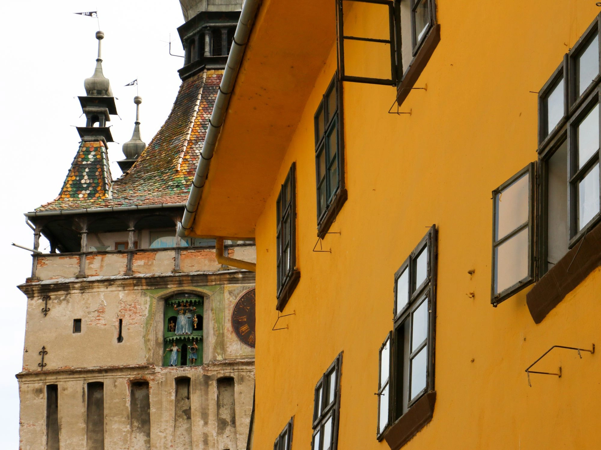 View of the medieval Clock Tower in Sighișoara, Romania behind bright yellow building
