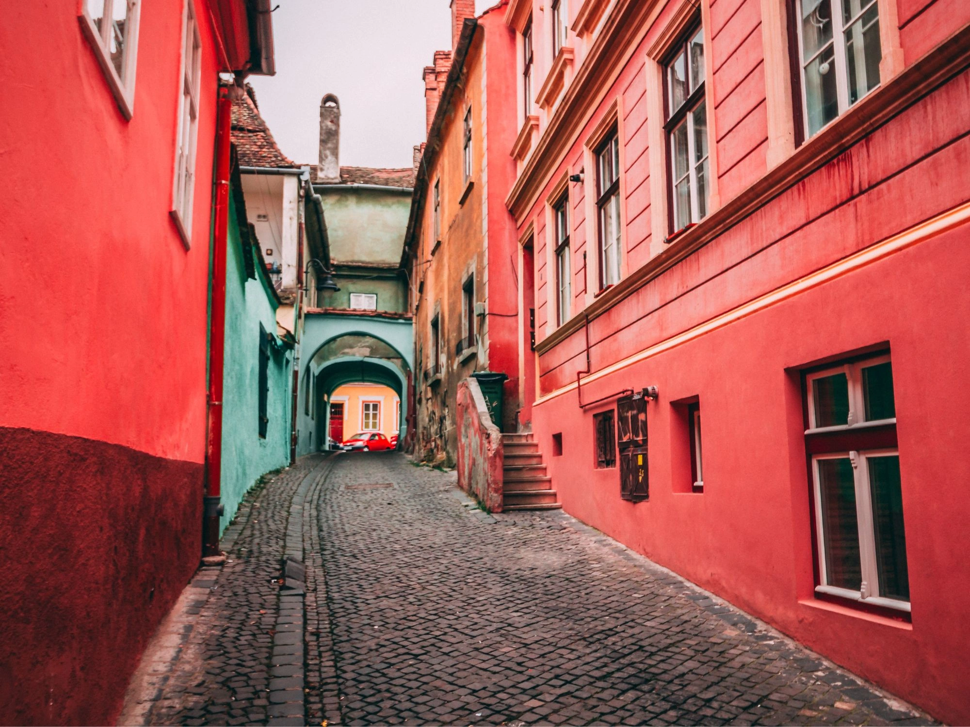 Colorful cobbled street in Sibiu, Romania, lined with red, green, and orange historic buildings.