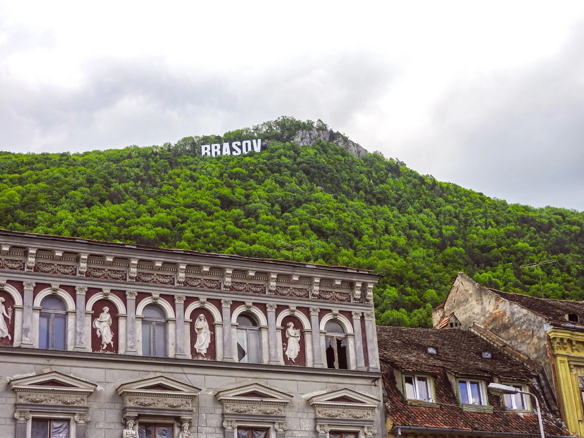 Hollywood-style Brasov sign on forested hill above old town buildings in Romania