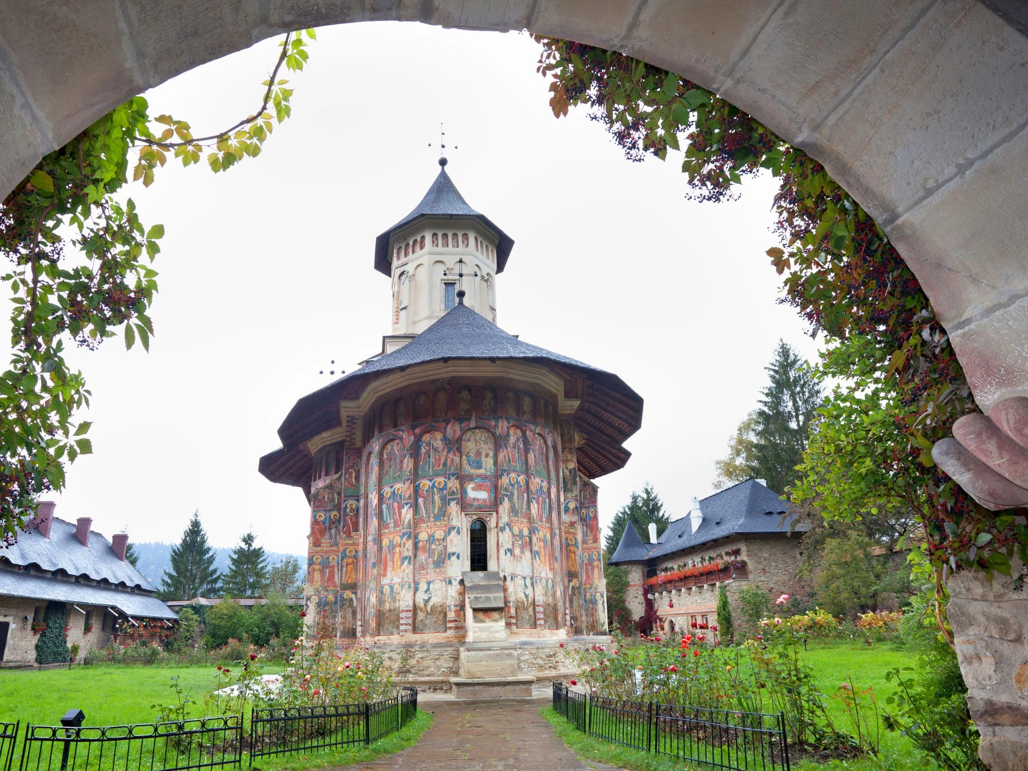 Bucovina monastery framed by a stone arch, with colorful frescoes and lush garden in the courtyard.