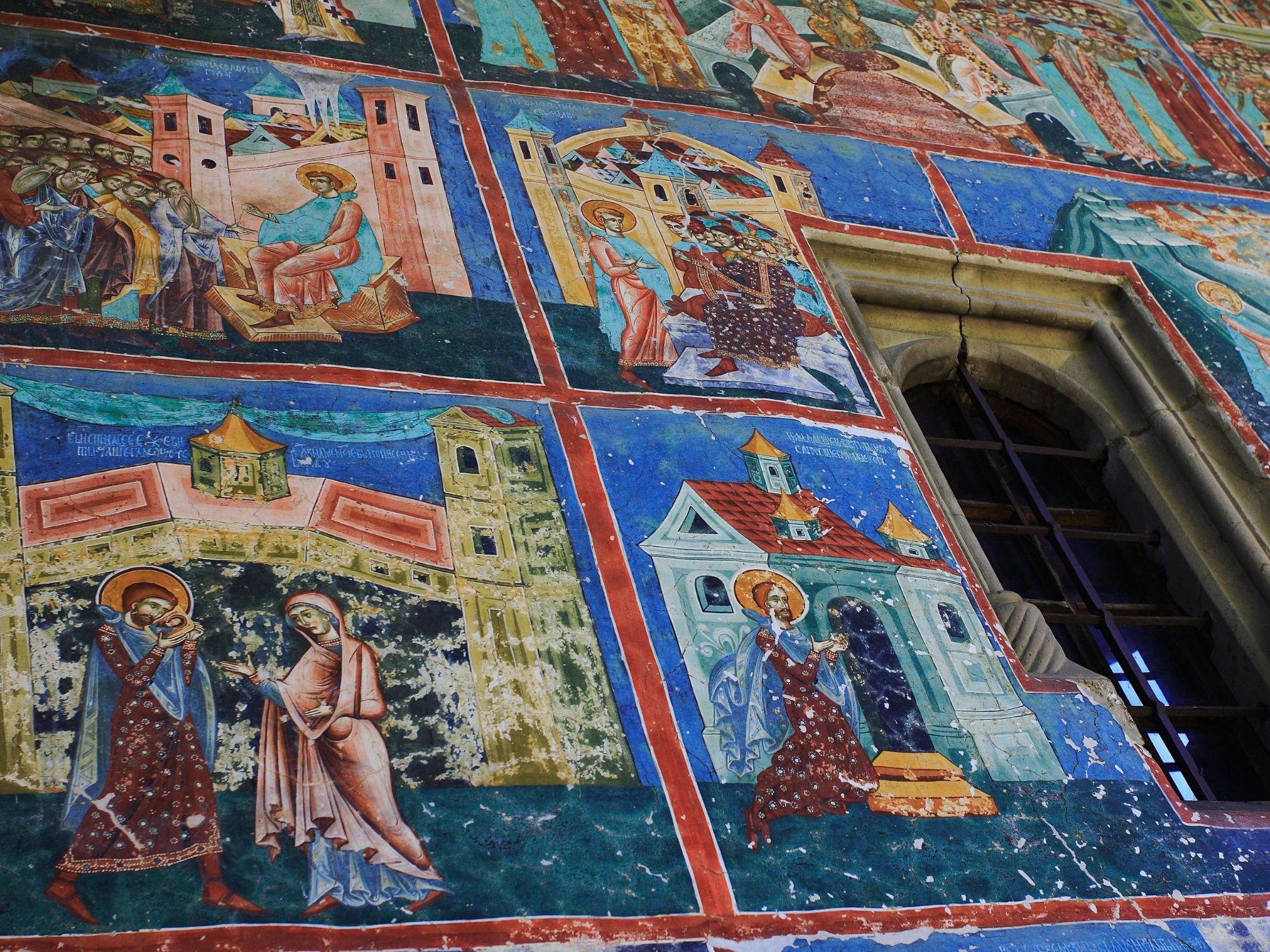 Romanian monastery wall with vibrant religious frescoes and detailed biblical scenes.