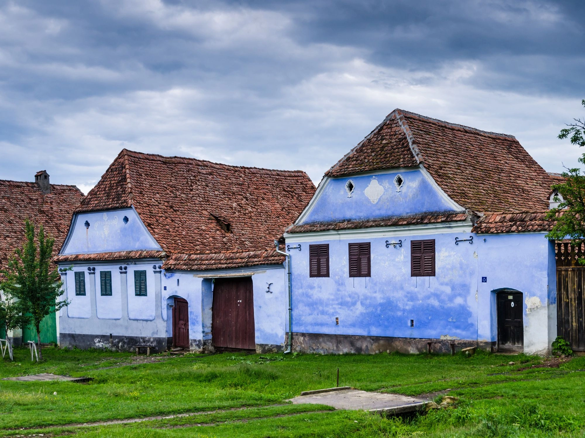 Traditional blue houses with red tiled roofs in a rural Romanian village under a cloudy sky.