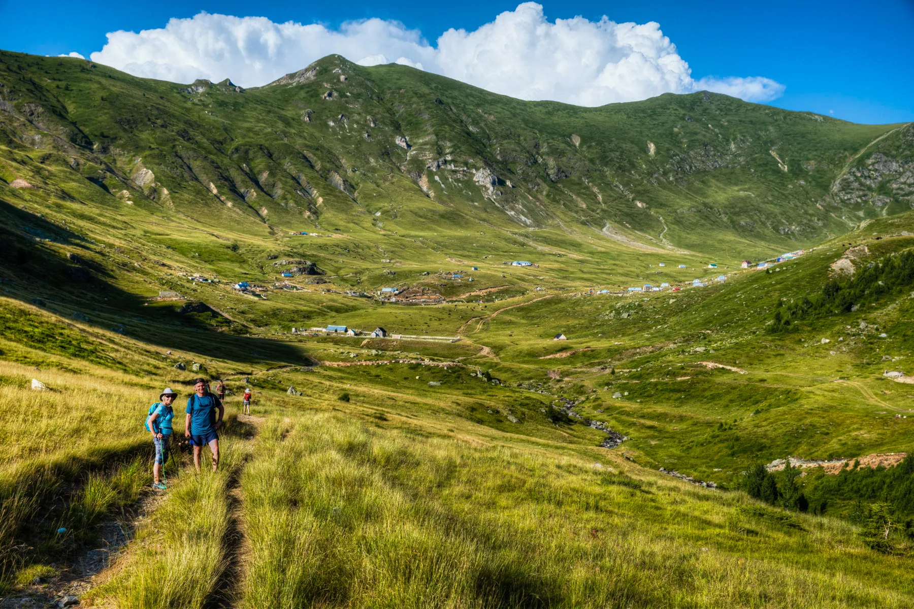 Hikers walking through the alpine village of Dobërdol on Kosovo’s Via Dinarica trail, with peaks behind.